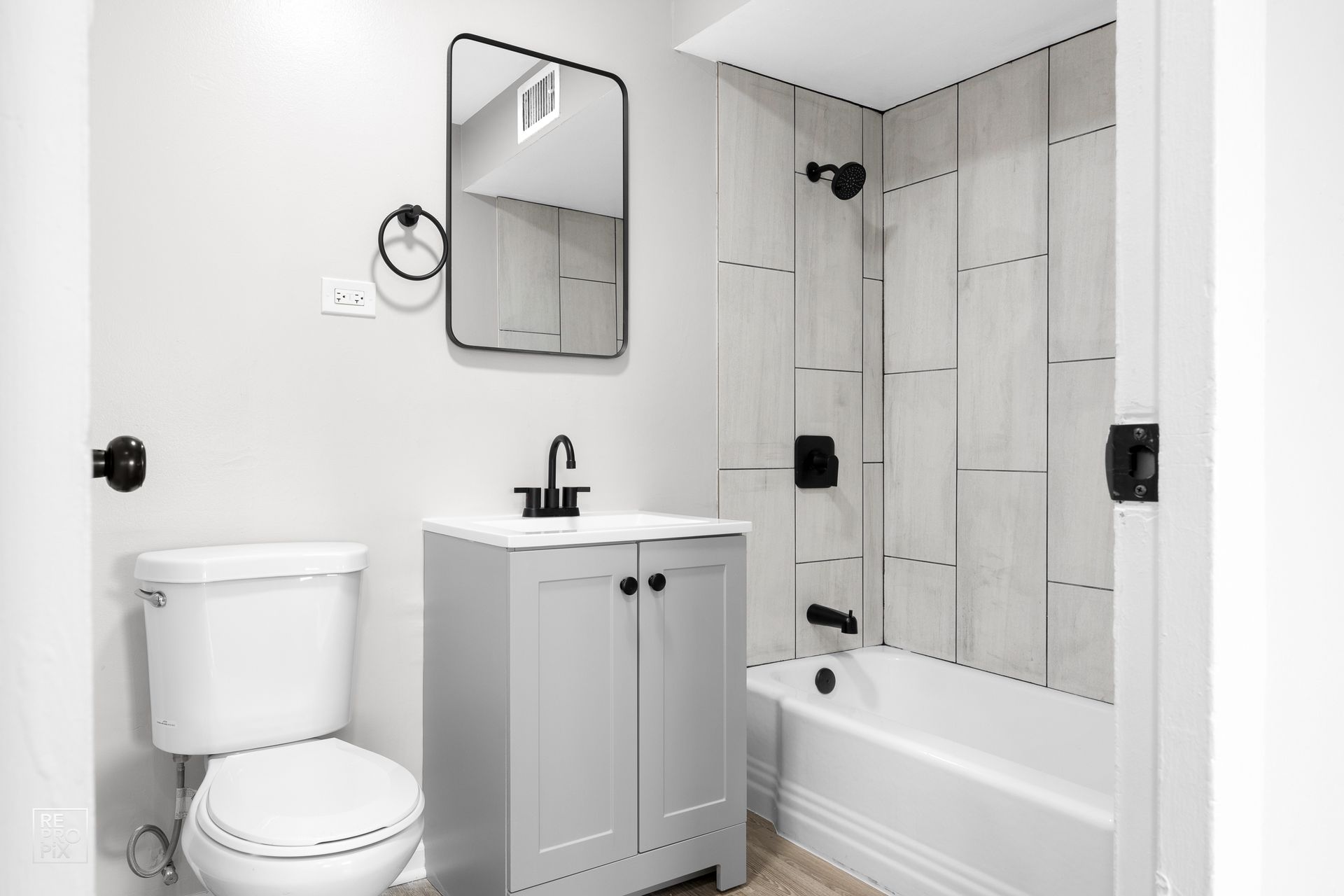 Small bathroom with a toilet, vanity, and shower. Black fixtures and gray and white tones.