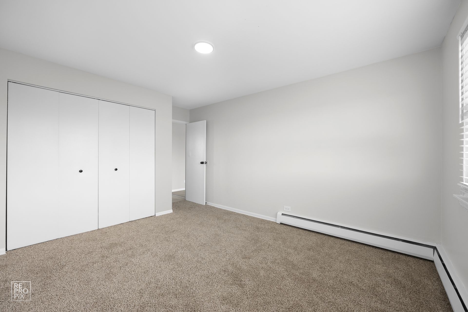 Empty bedroom with beige carpet, white walls, closet, and a doorway.