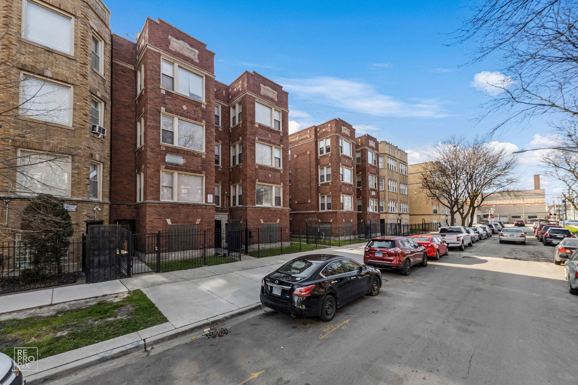 Apartment buildings on a city street; cars parked along the curb on a sunny day.