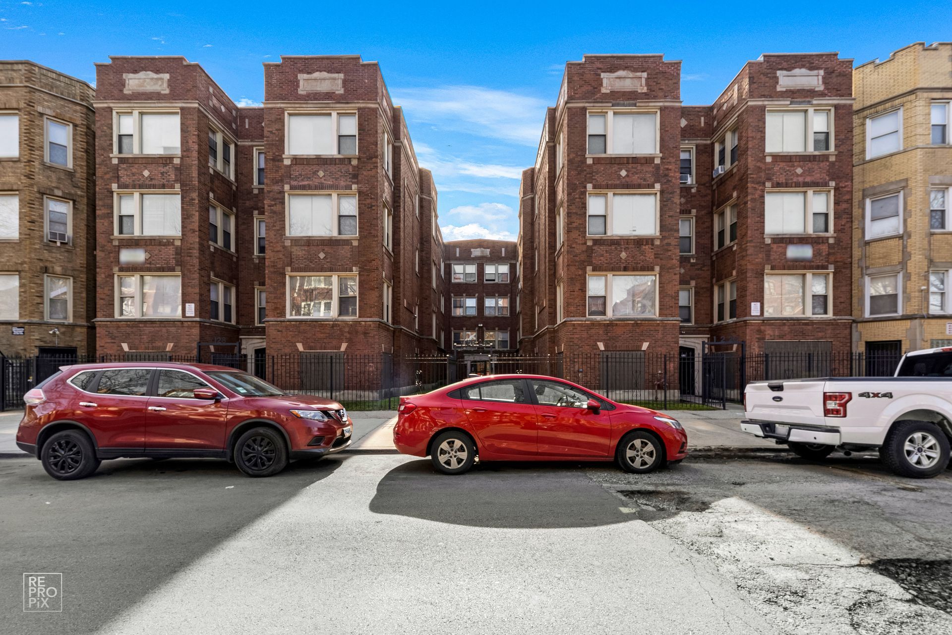 Apartment buildings with cars parked in front on a sunny day.
