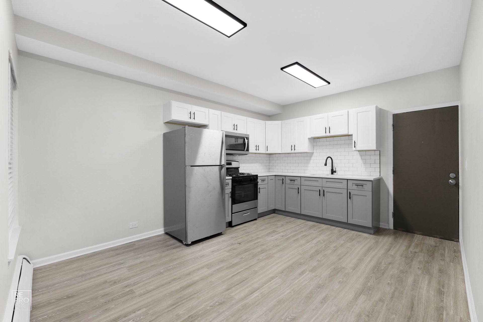 Empty kitchen with stainless steel appliances, light gray cabinets, and laminate flooring.
