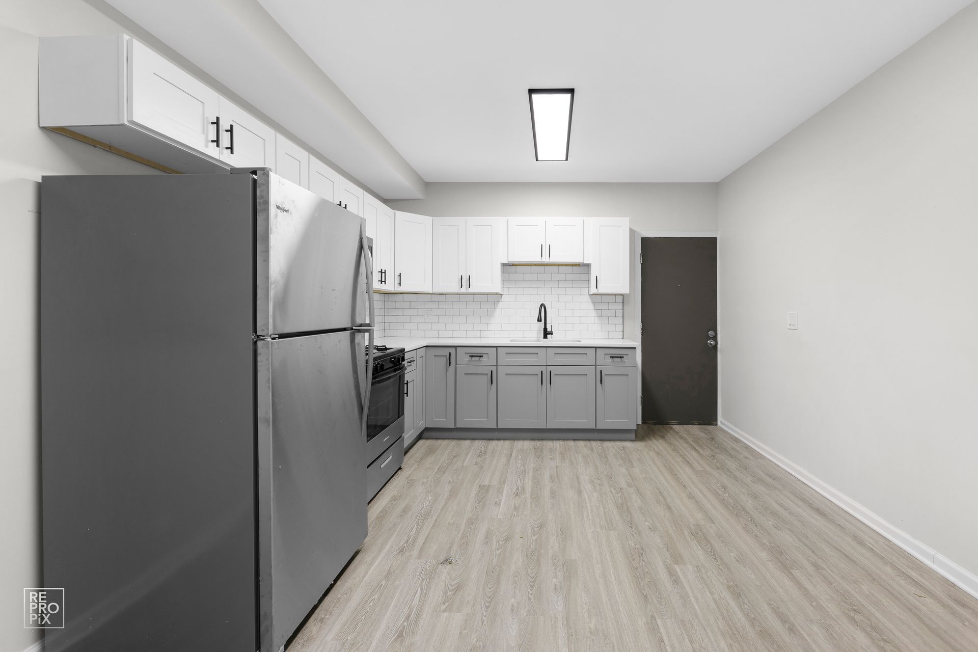 Modern kitchen with gray and white cabinets, stainless steel appliances, and light wood-look flooring.