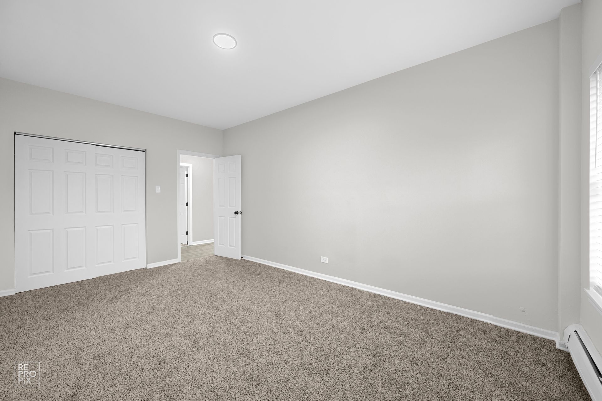 Empty bedroom with gray walls, beige carpet, closed closet, and open doorway.
