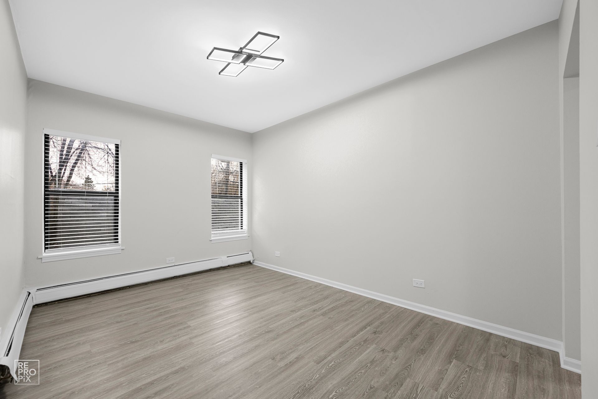 Empty room with gray walls, wood-look flooring, two windows, and modern ceiling light.