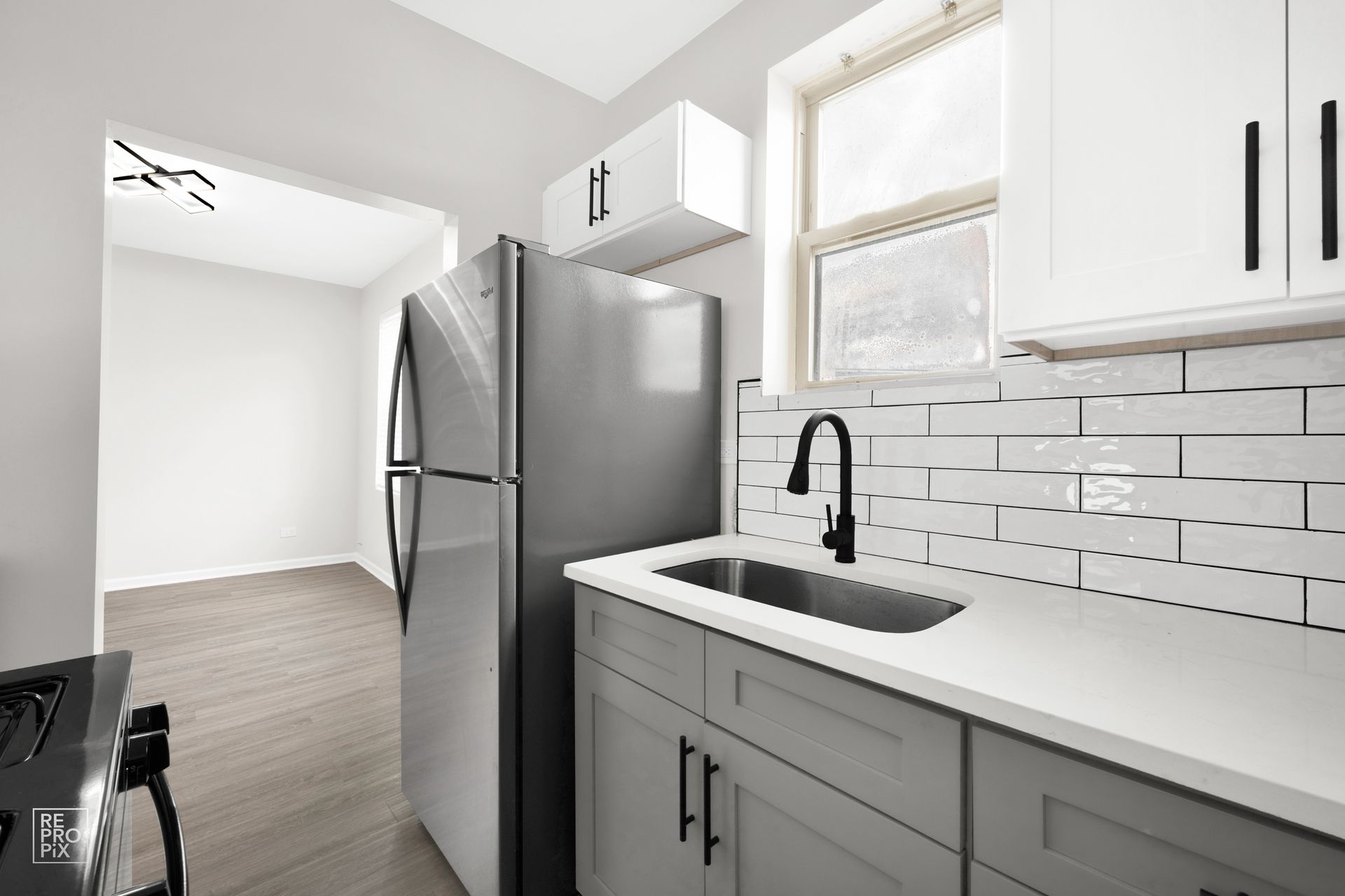 Kitchen with stainless steel refrigerator, gray cabinets, white subway tile backsplash, and a window.
