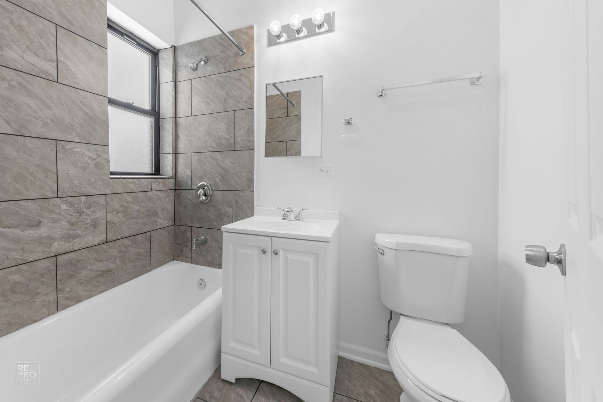 Bathroom with white toilet, vanity, and tub; gray tile accents.