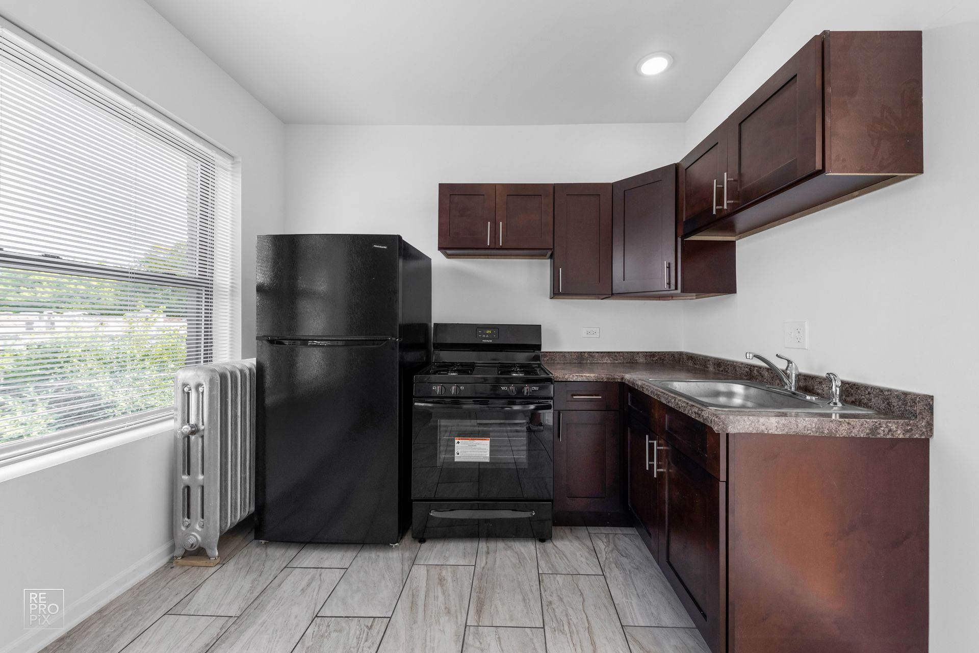 Small kitchen with dark cabinets, black appliances, and a window.