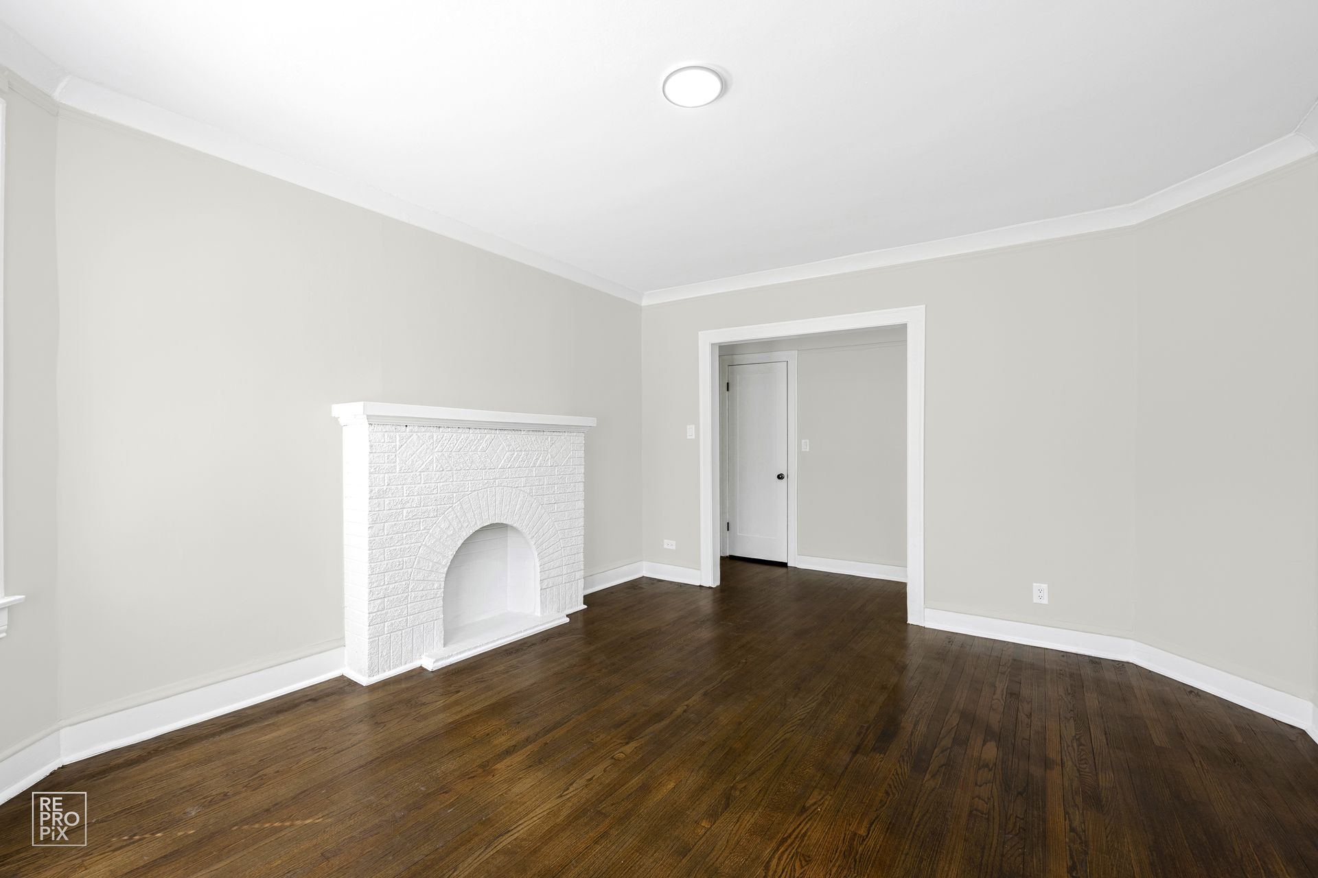 Empty room with dark wood floors, white fireplace, and doorway.