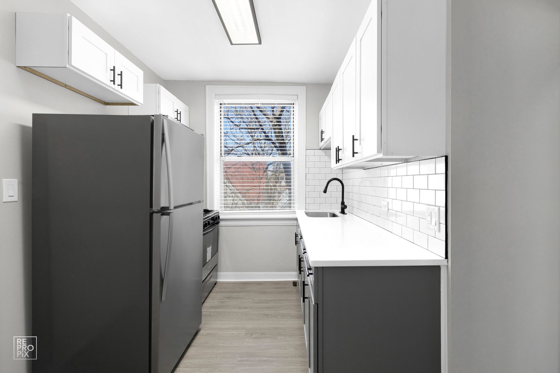 Modern galley kitchen with gray cabinets, white countertops, and a black refrigerator.