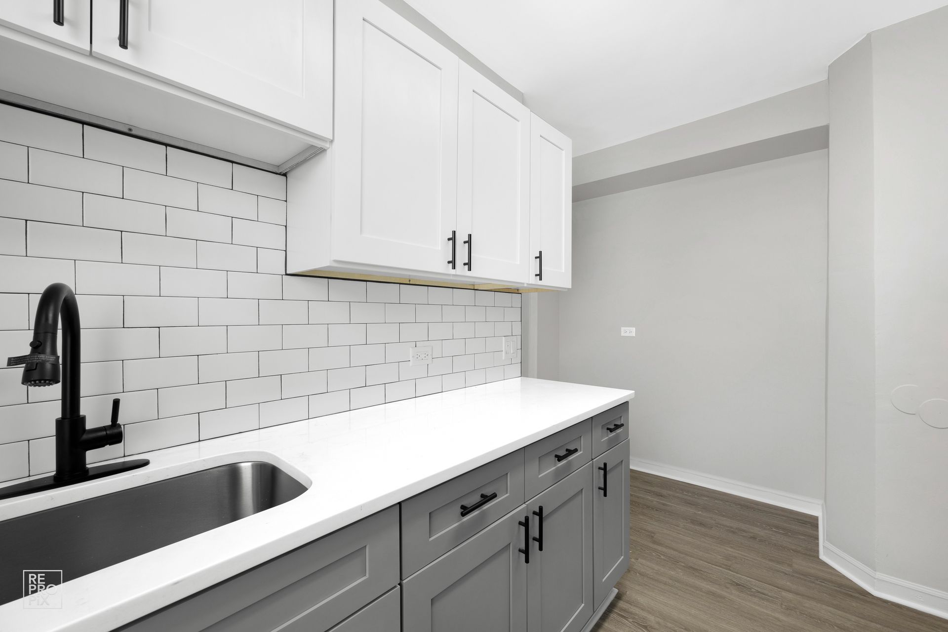 Kitchen with white and gray cabinets, subway tile backsplash, and stainless steel sink.