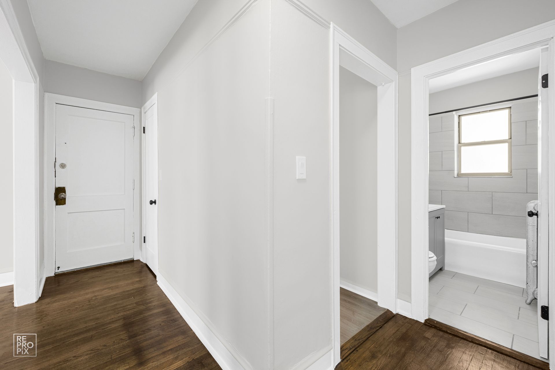 Hallway with dark wood floors, white walls, and doorways leading to rooms.