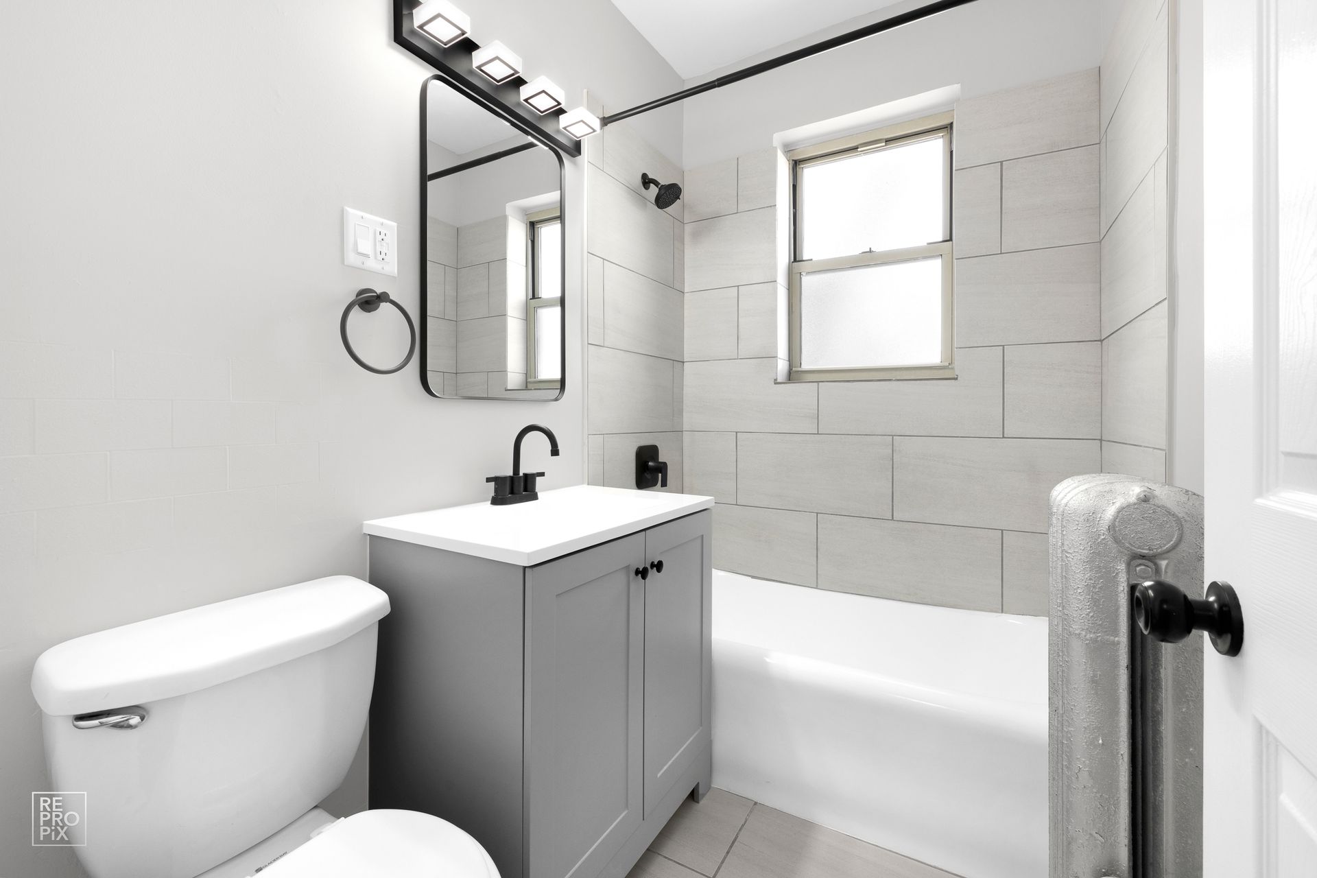 Gray and white bathroom with a toilet, vanity, bathtub, and window.