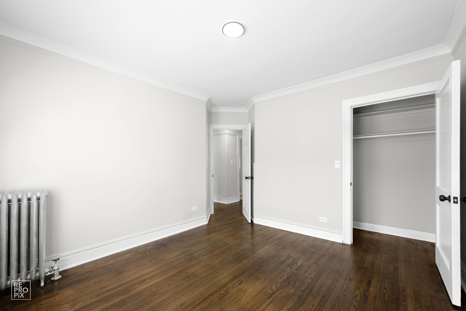 Empty room with hardwood floors, white walls, and a closet. Radiator visible.