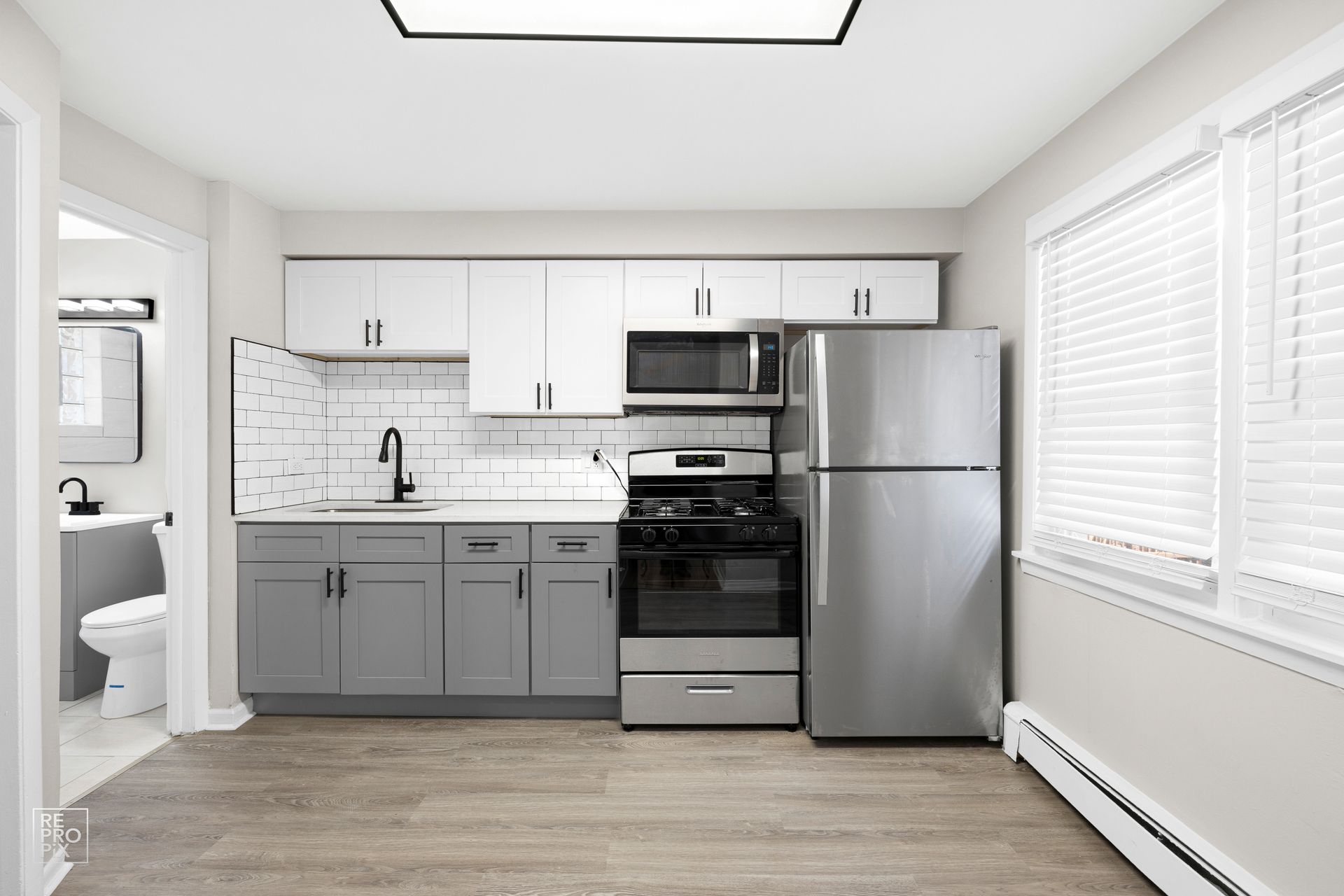 Kitchen with gray and white cabinets, stainless steel appliances, and a window with blinds.