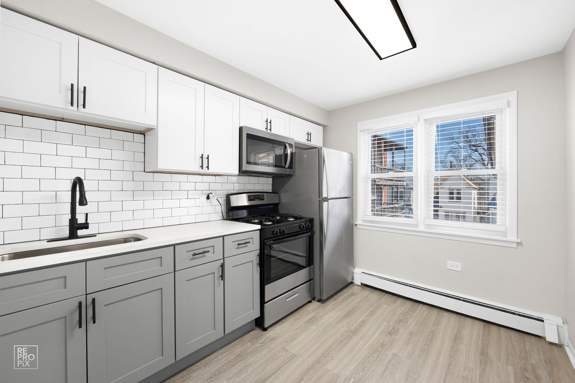 Modern kitchen with gray and white cabinets, stainless steel appliances, and a window.