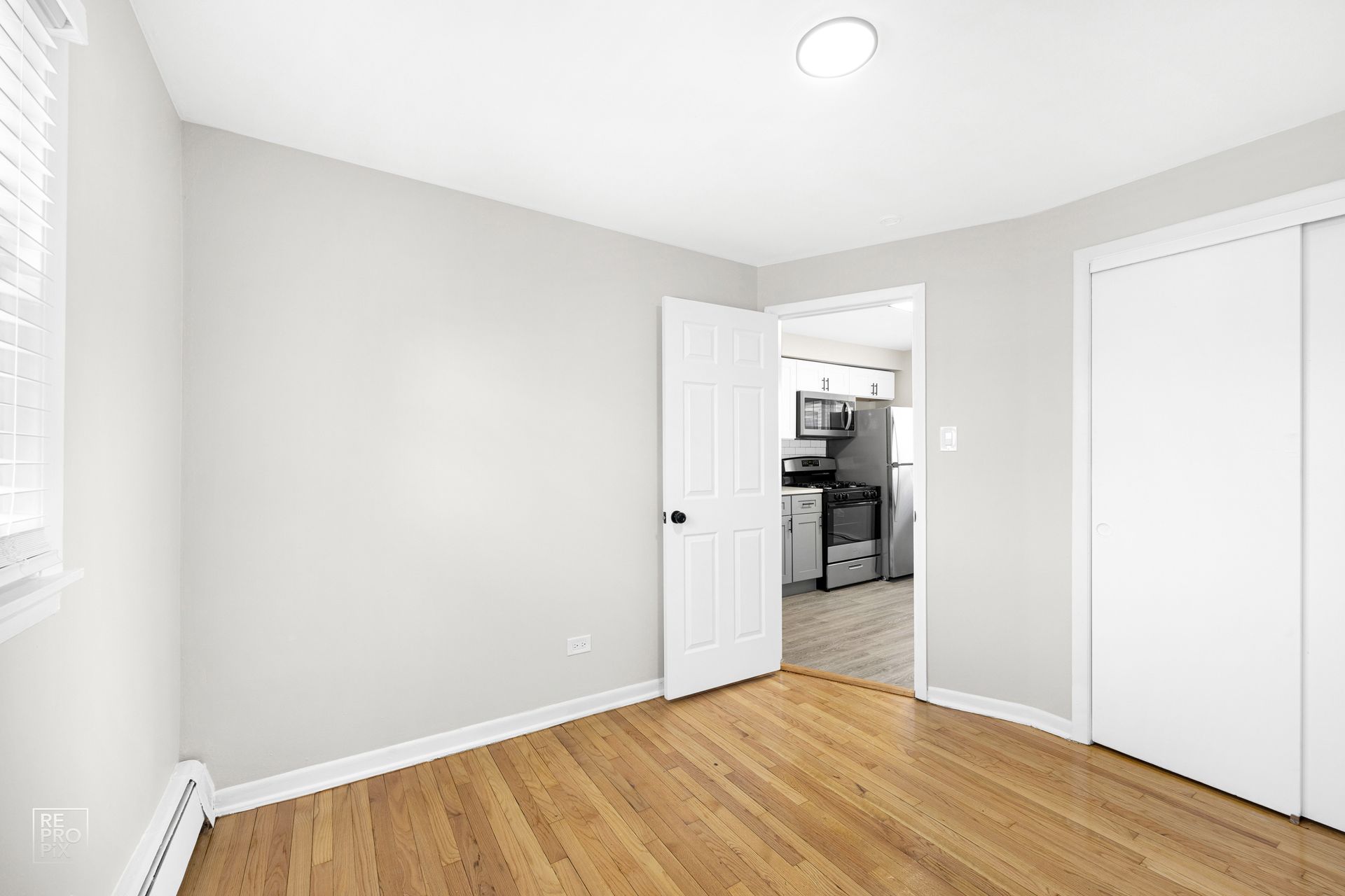 Empty room with wood floors, white walls, closet, and doorway leading to a kitchen.