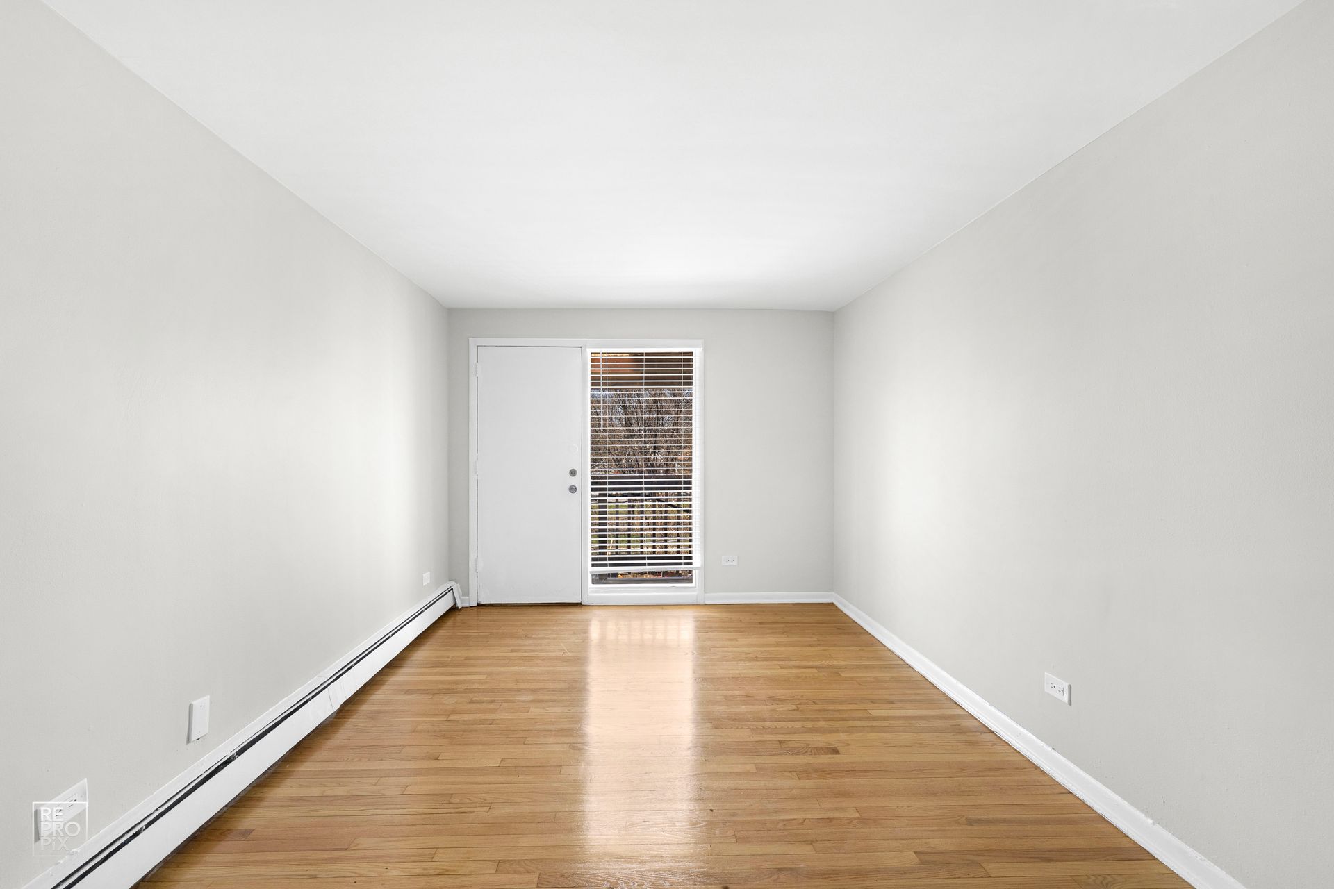 Empty room with hardwood floors, light gray walls, and a door to the outside.