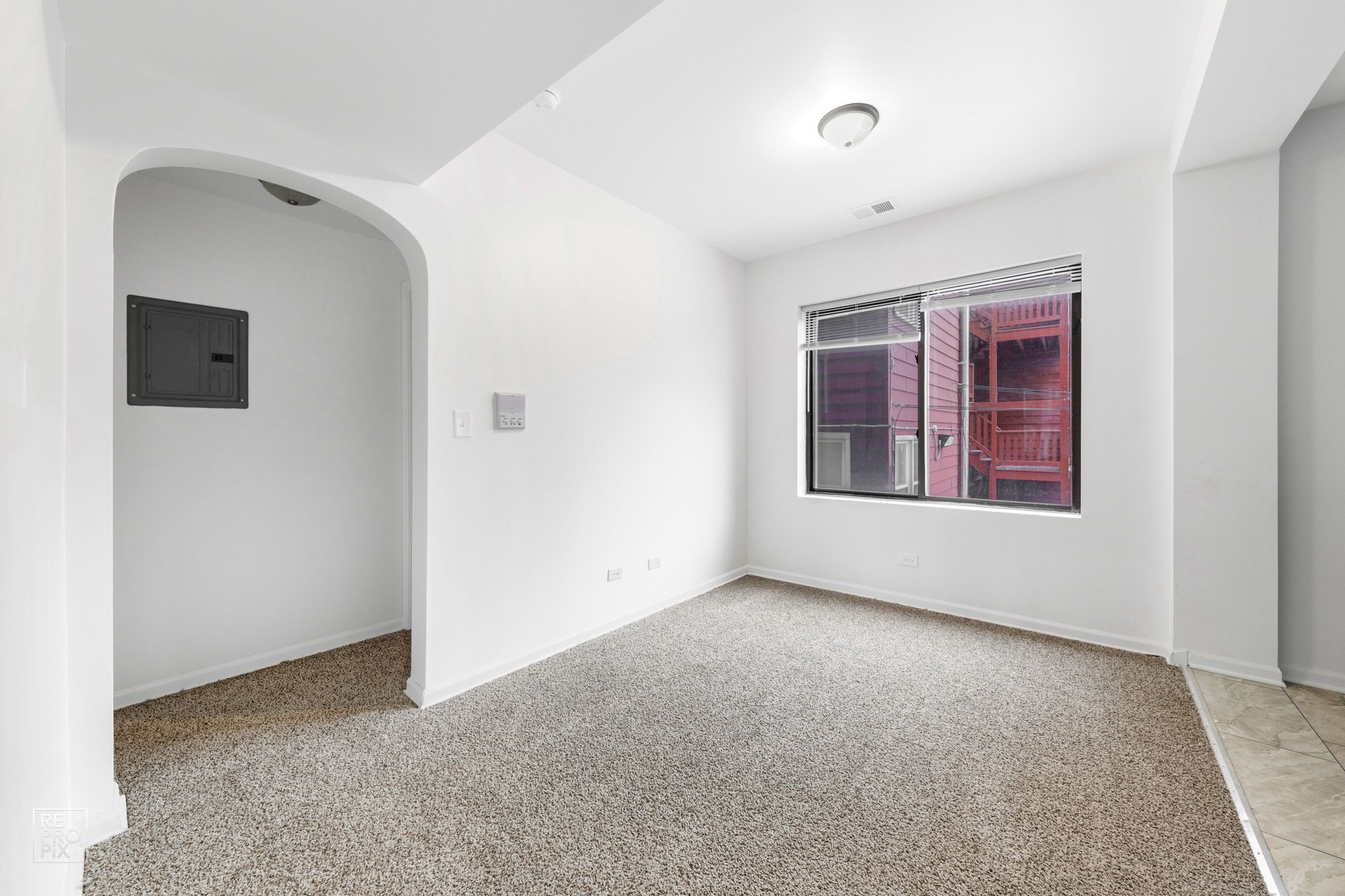 Empty room with beige carpet, arched doorway, and a window with red exterior visible.
