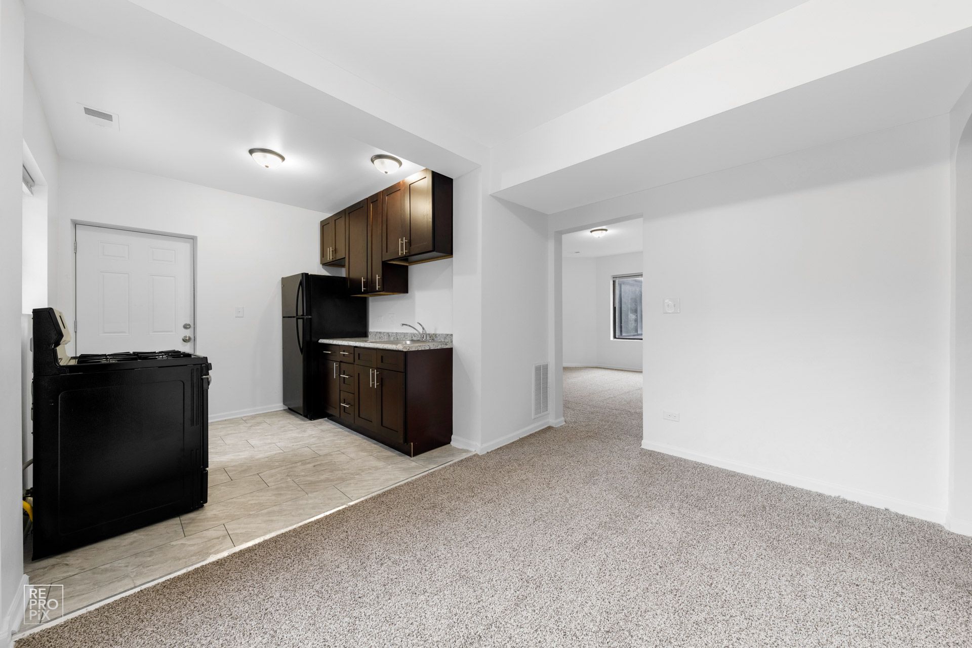 Kitchen with dark cabinets, black appliances, and beige carpet.