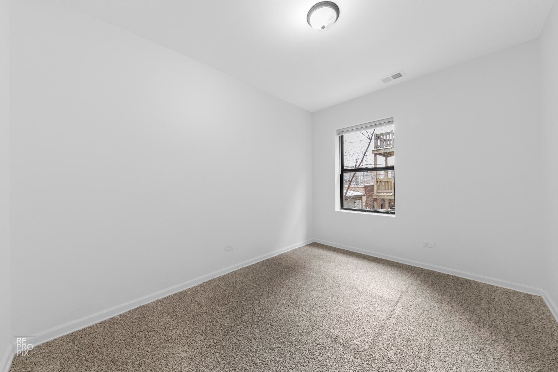 Empty room with white walls, carpeted floor, window, and ceiling light.