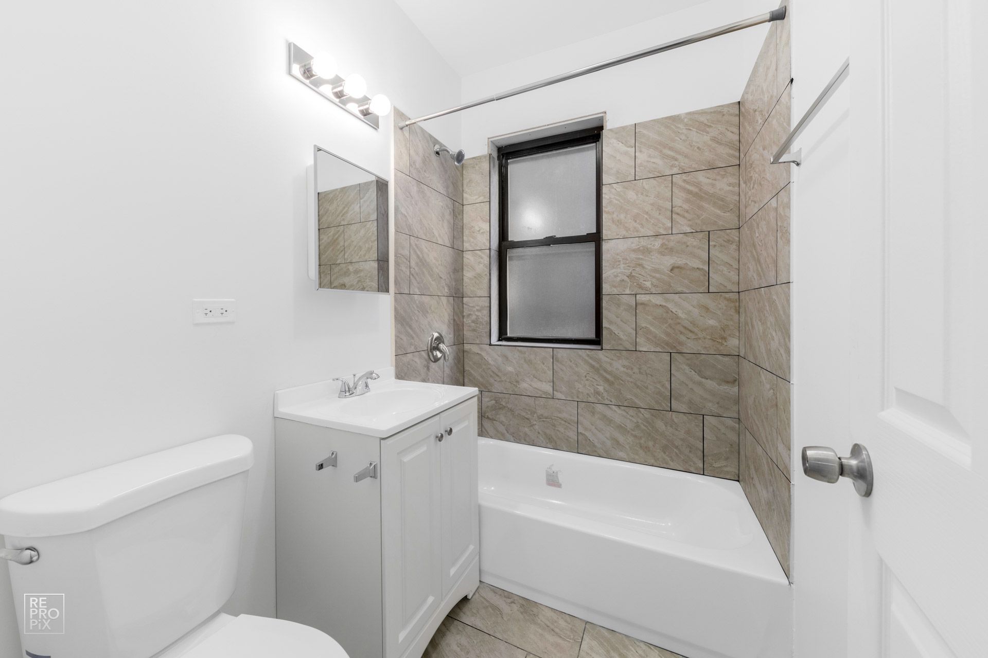 Bathroom with white fixtures, beige tile, and a small window above the tub.