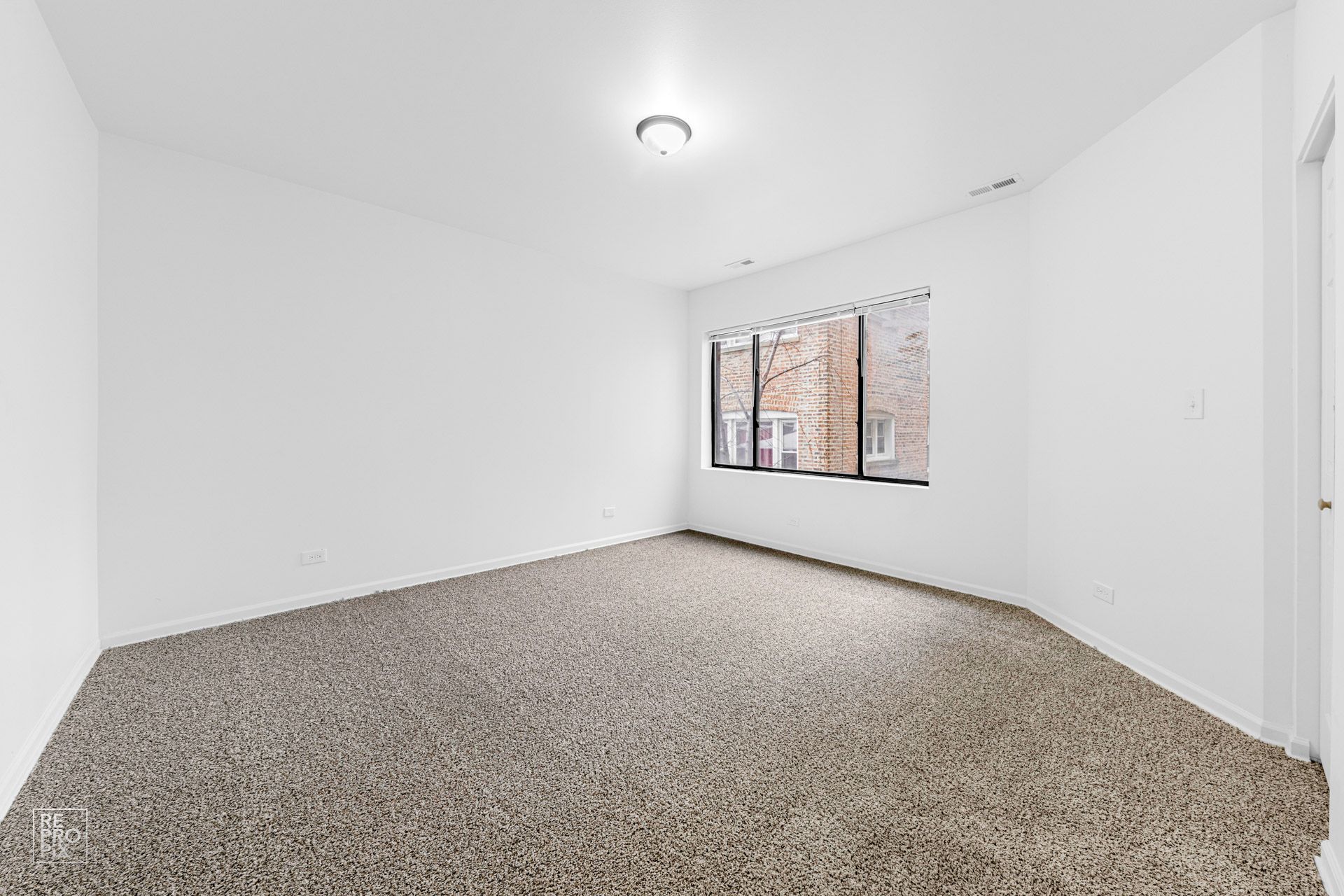 Empty room with white walls, brown carpet, window, and ceiling light.