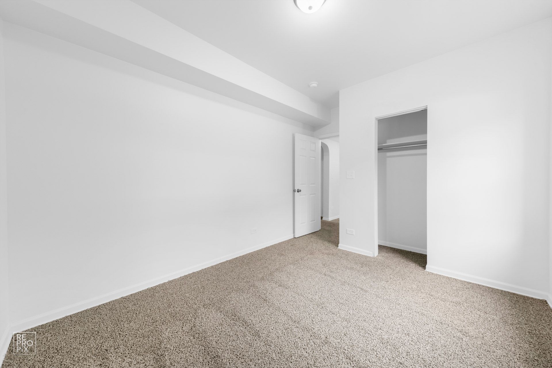 Empty white bedroom with carpet, closet, and a doorway.