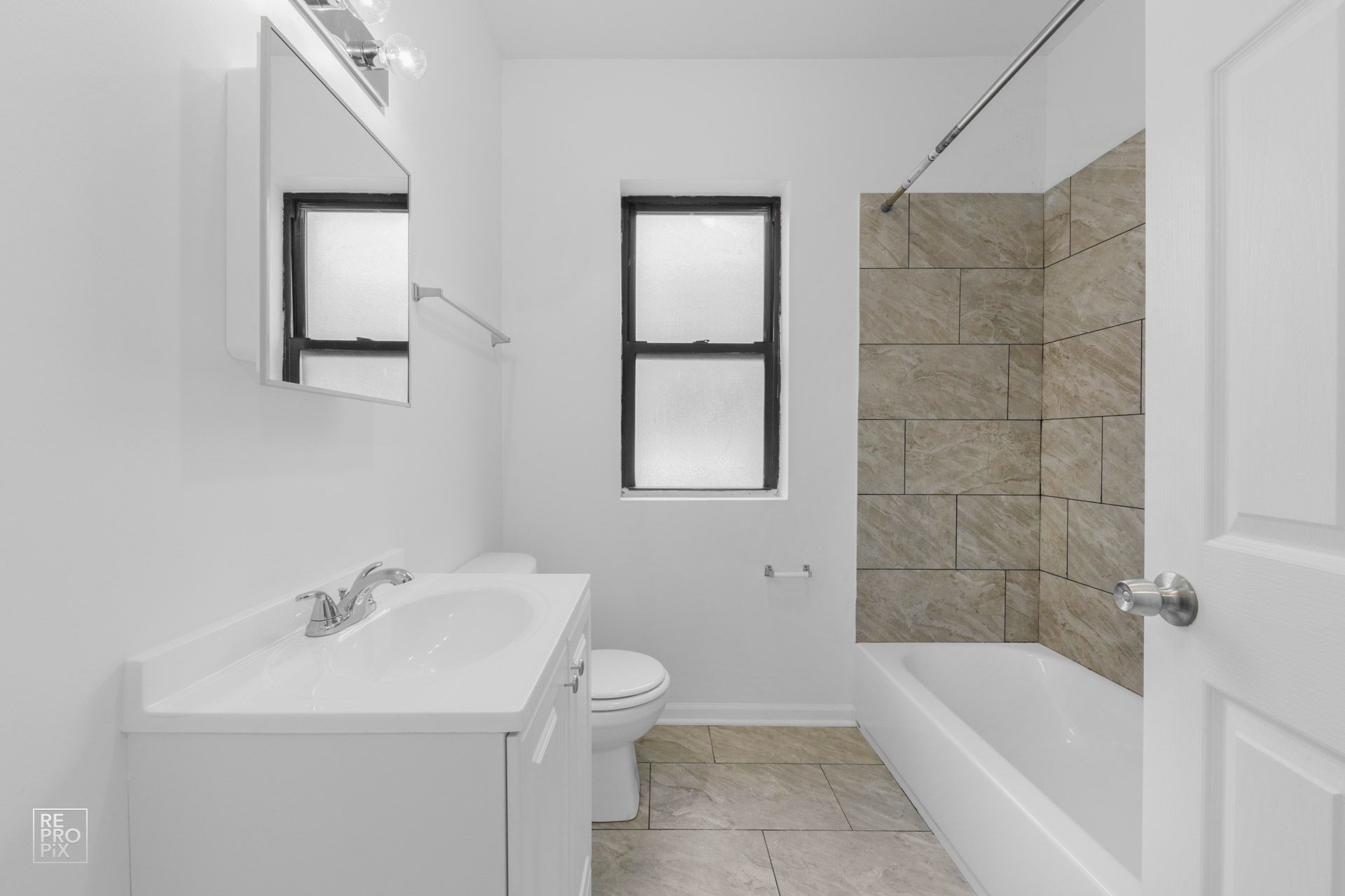 White bathroom with a sink, toilet, tub, and window. Tile accent wall.