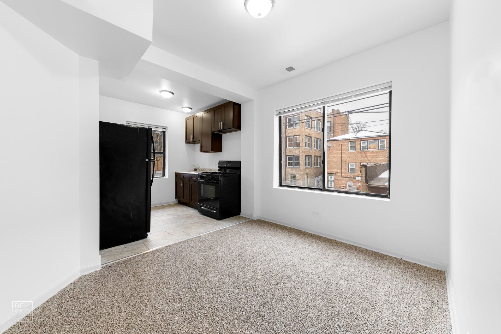 Empty kitchen area with black appliances, brown cabinets, and a window overlooking a city.