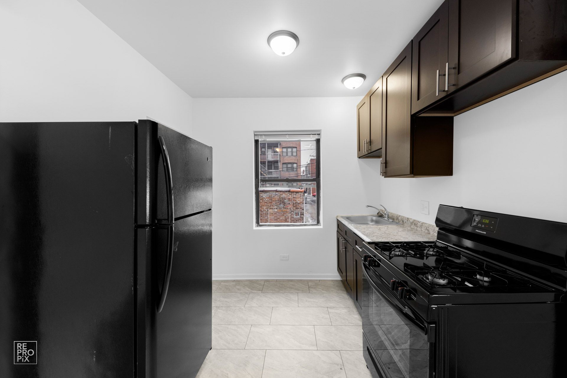 Black kitchen with fridge, stove, cabinets, and a window.