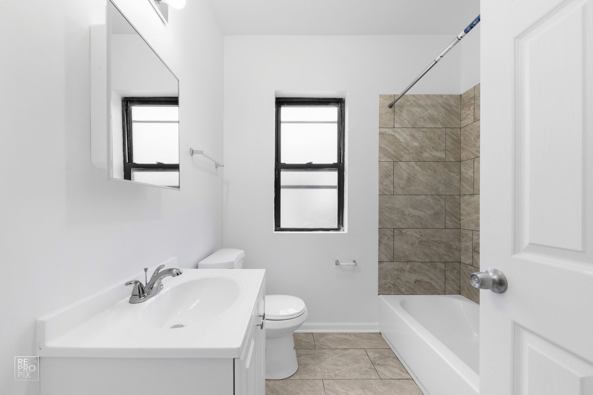 White bathroom with sink, toilet, tub, window, and mirror.
