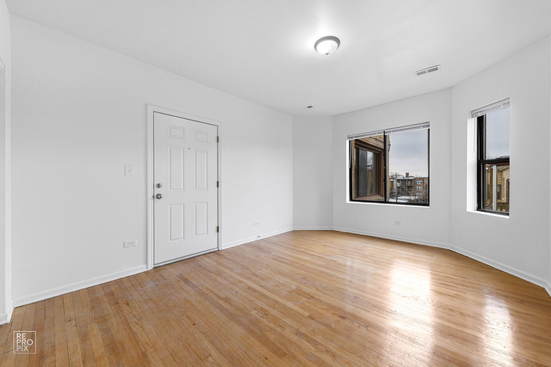 Empty room with wood floors, white walls, a door, and two windows.