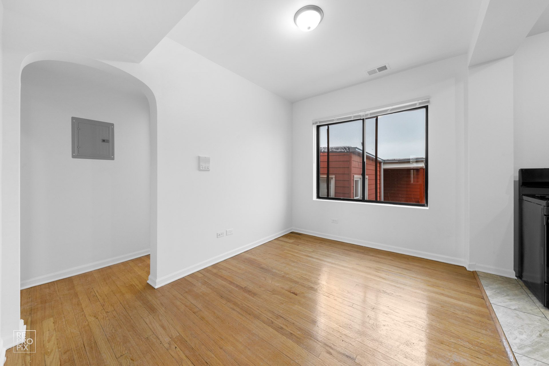 Empty room with hardwood floors, white walls, and a window.