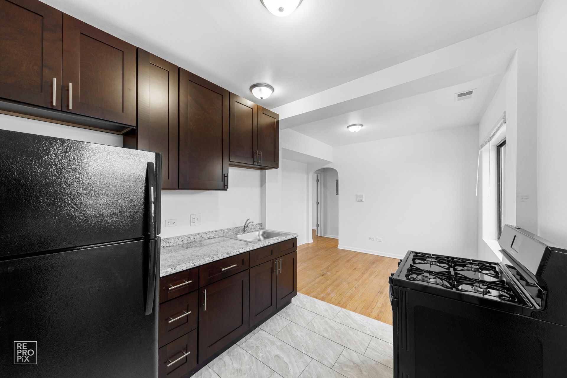 Kitchen with dark brown cabinets, black appliances, white countertops, and hardwood floors.