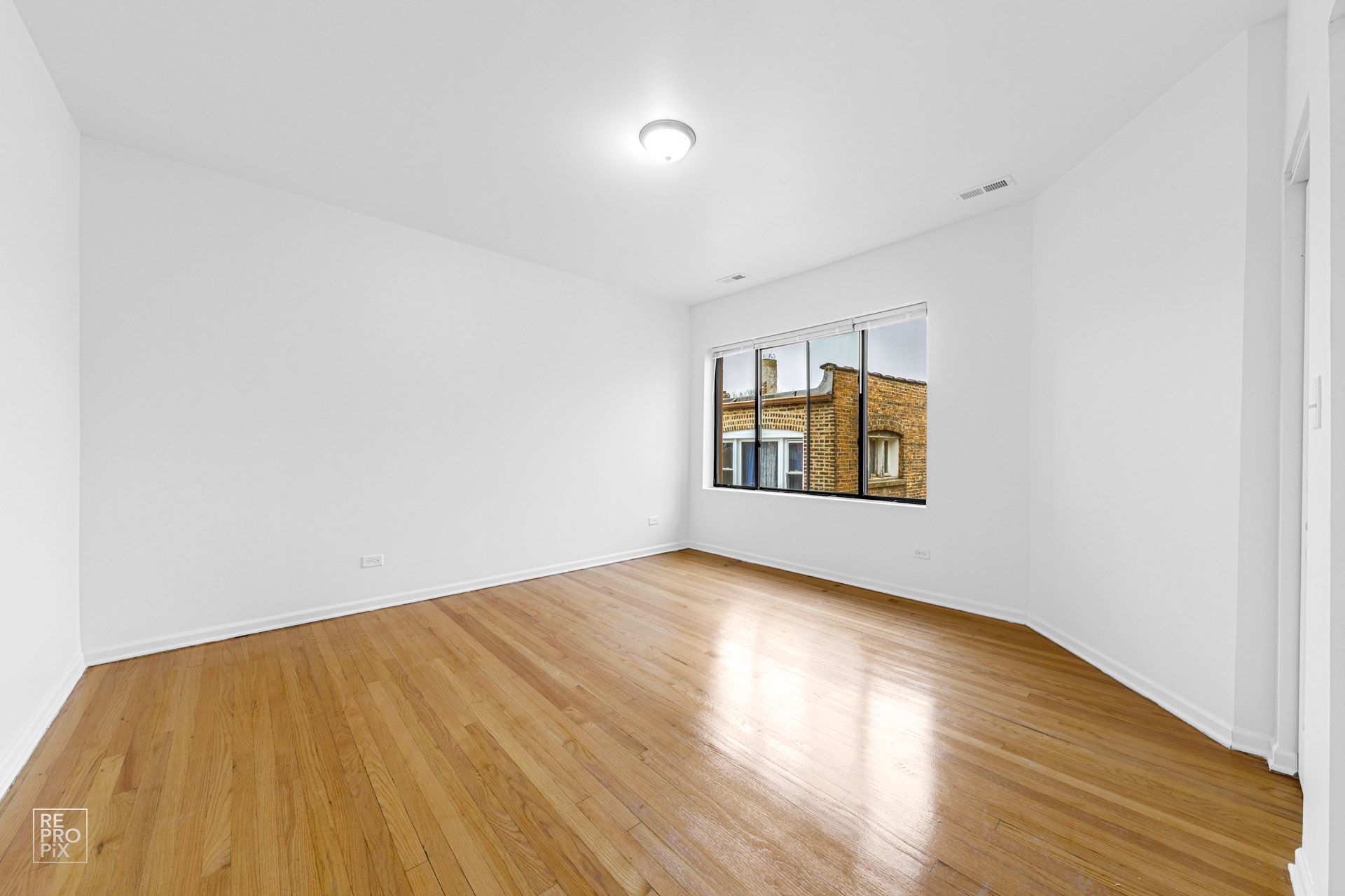 Empty room with wood floors, white walls, and a window with a building view.
