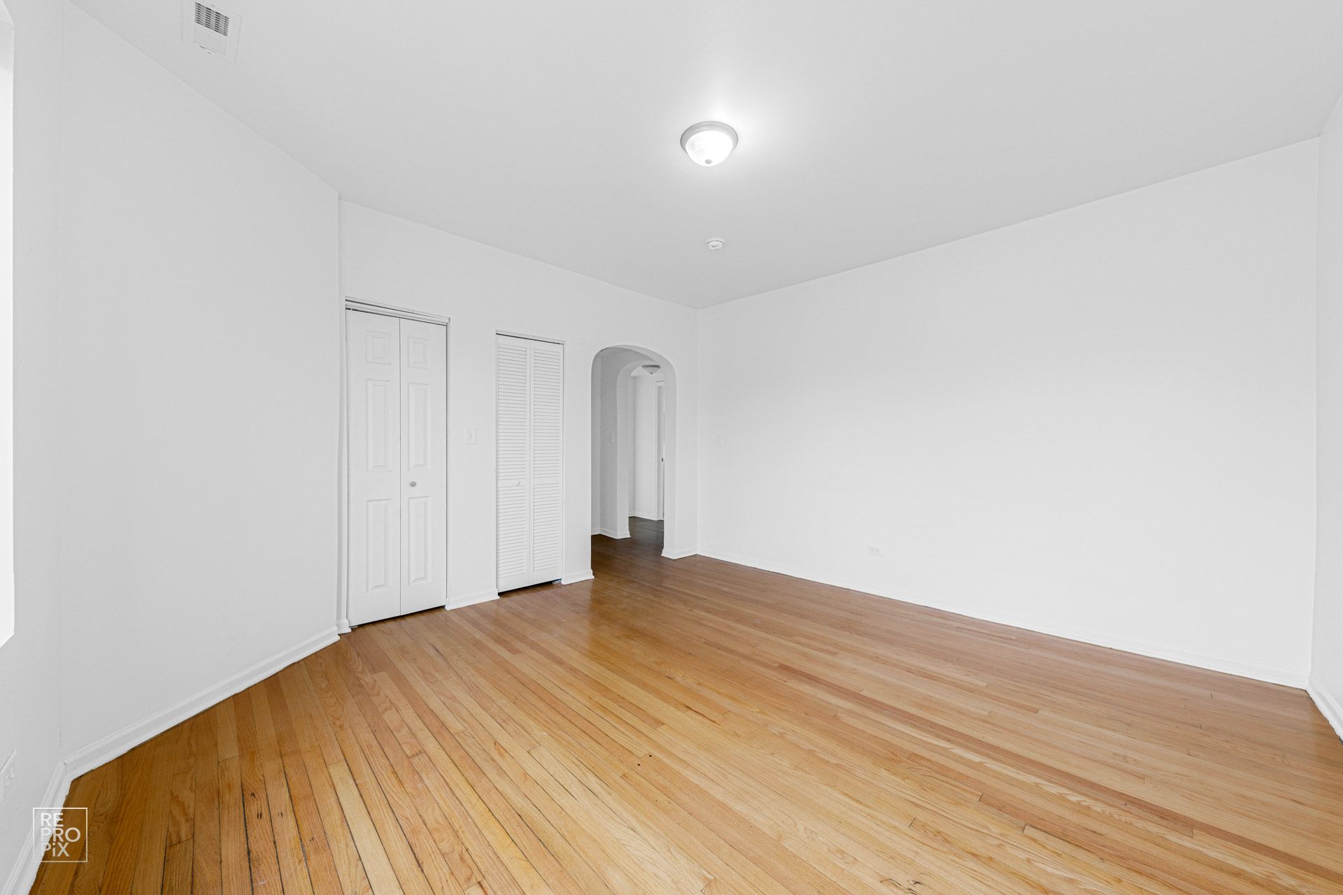 Empty room with hardwood floors, white walls, two closets, and an arched doorway.