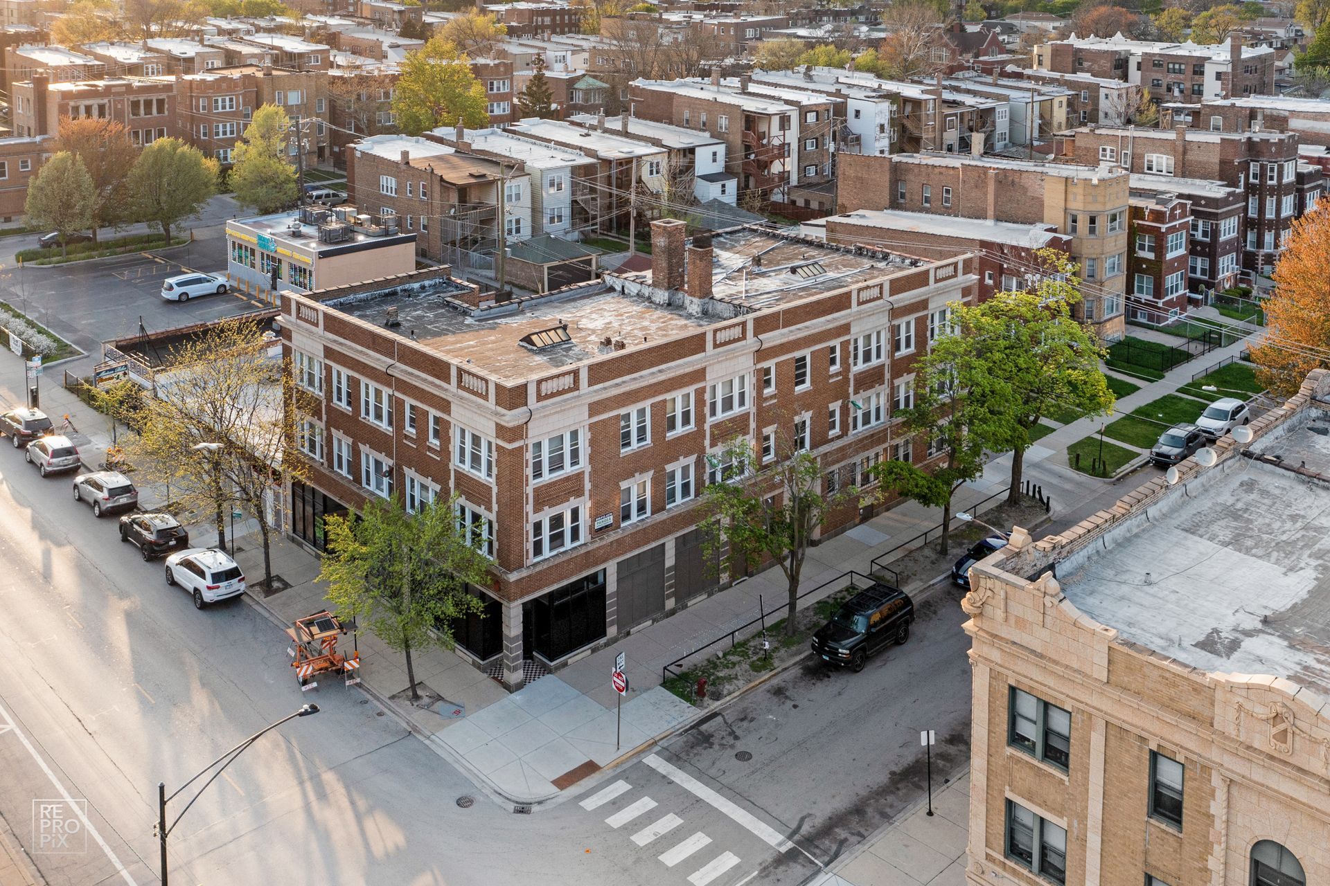 Aerial view of a three-story brick apartment building on a city street; cars parked along the street.