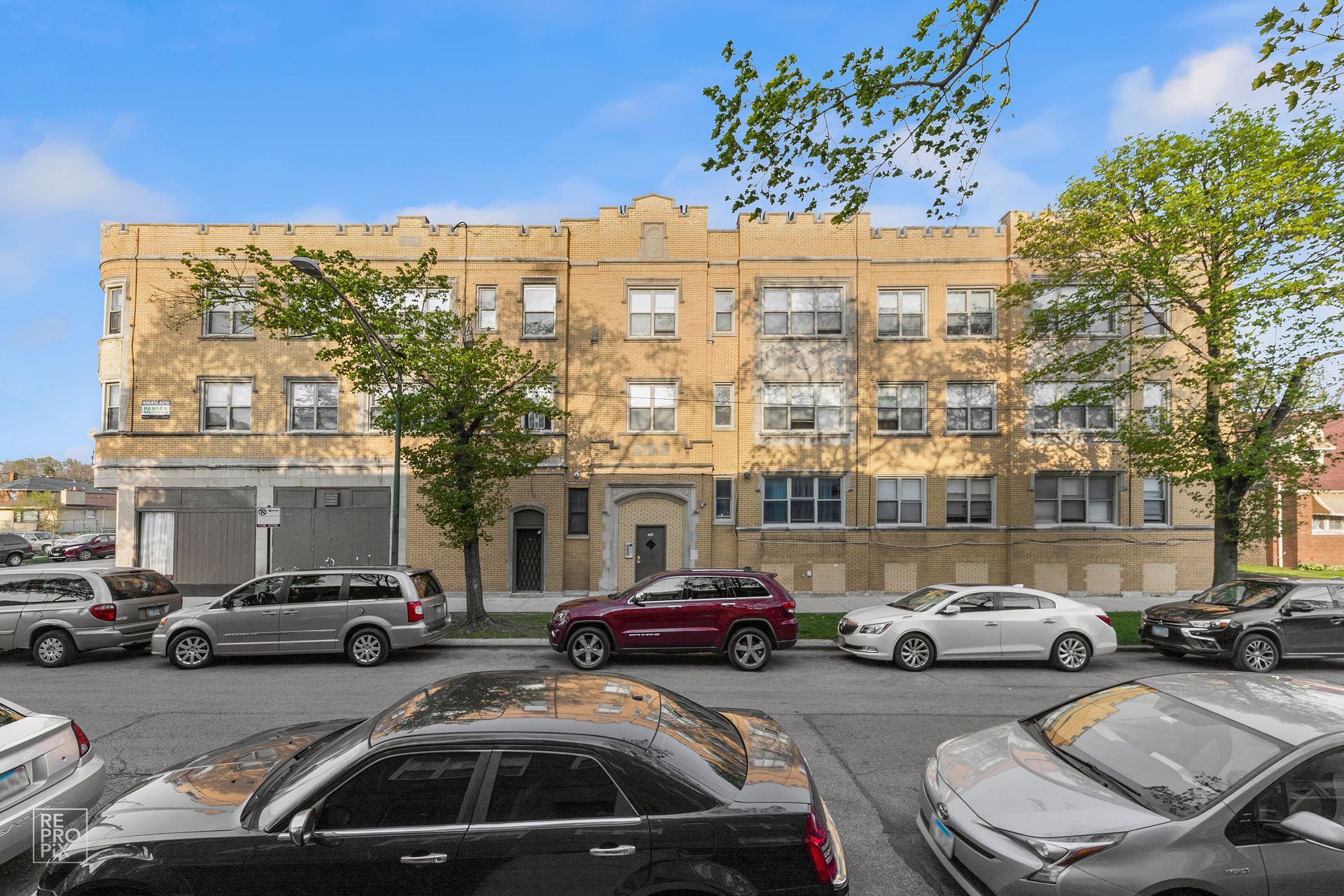 Apartment building on a city street, tan brick with parked cars in front.