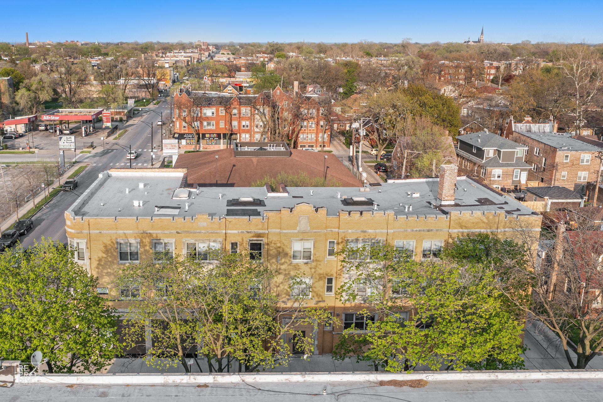 Aerial view of an apartment building with tan facade, trees, and cityscape in the background.