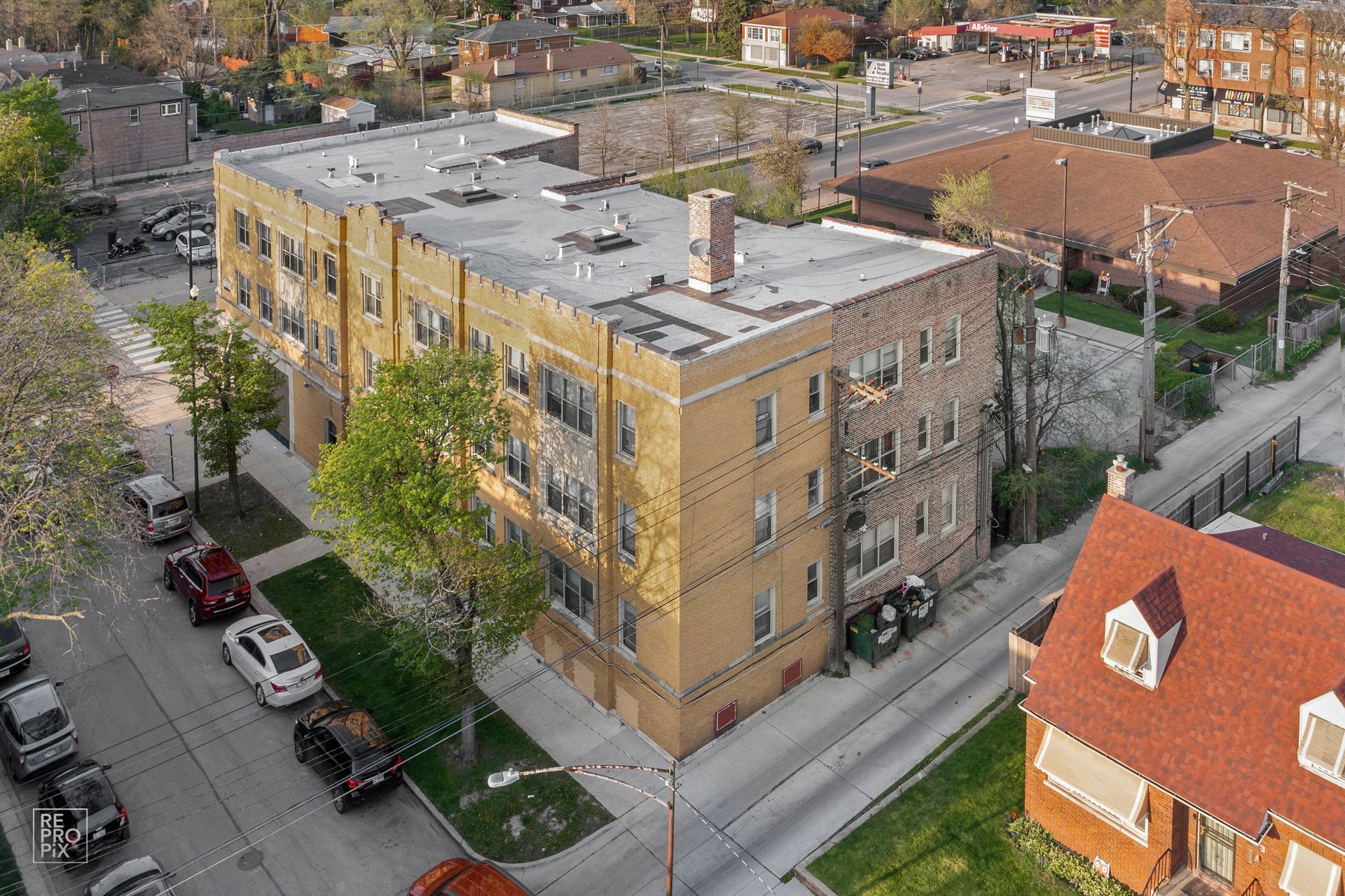 Aerial view of a multi-story brick apartment building with cars parked on the street.