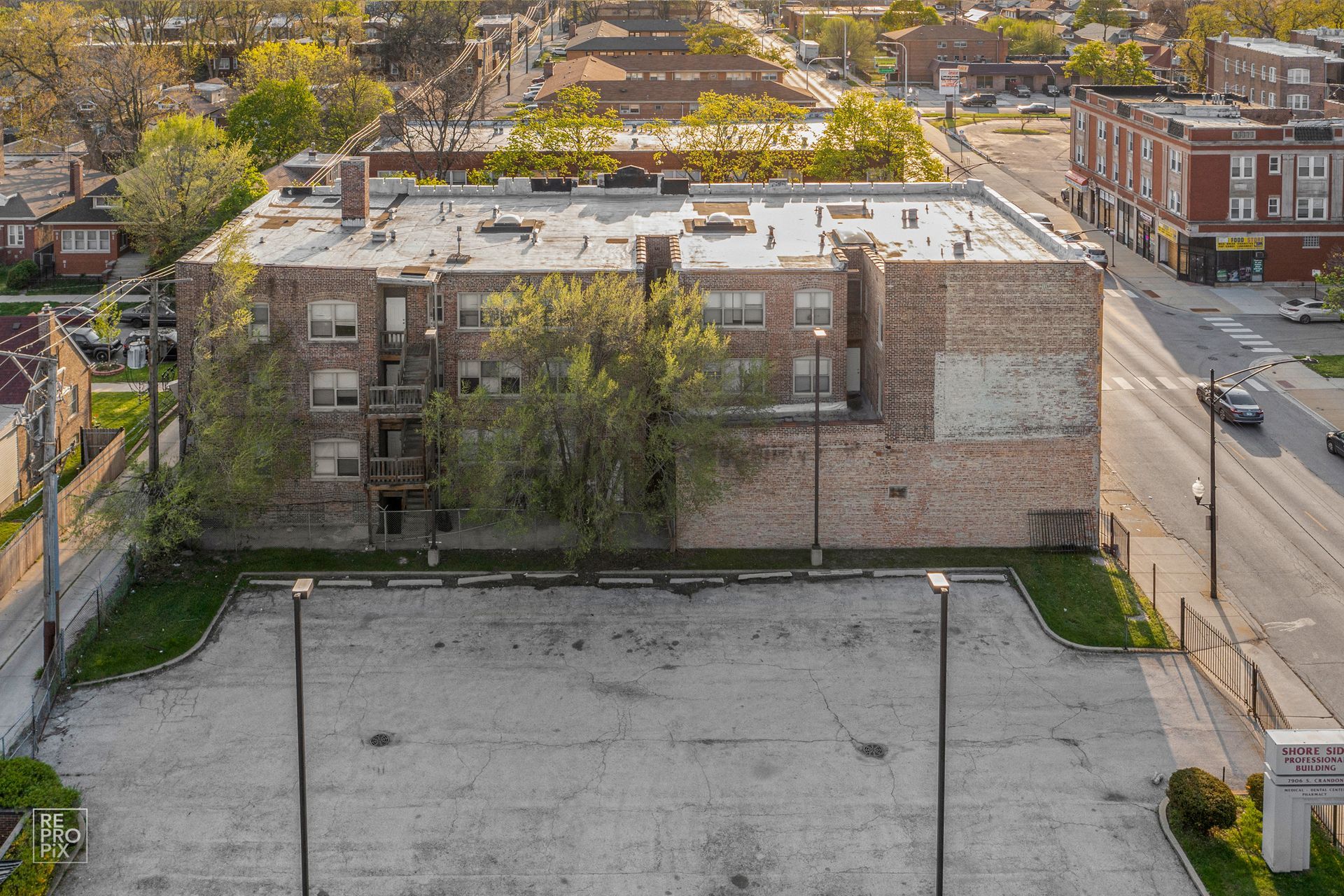 Aerial view of a brick apartment building with a parking lot in front and street on the right.