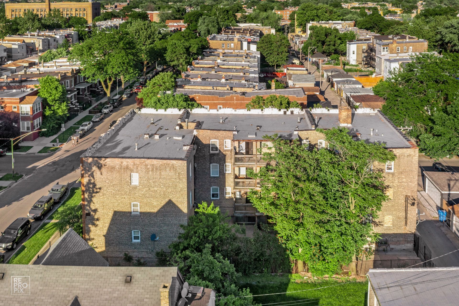 Aerial view of multi-unit brick building with rooftops and trees in a residential neighborhood.