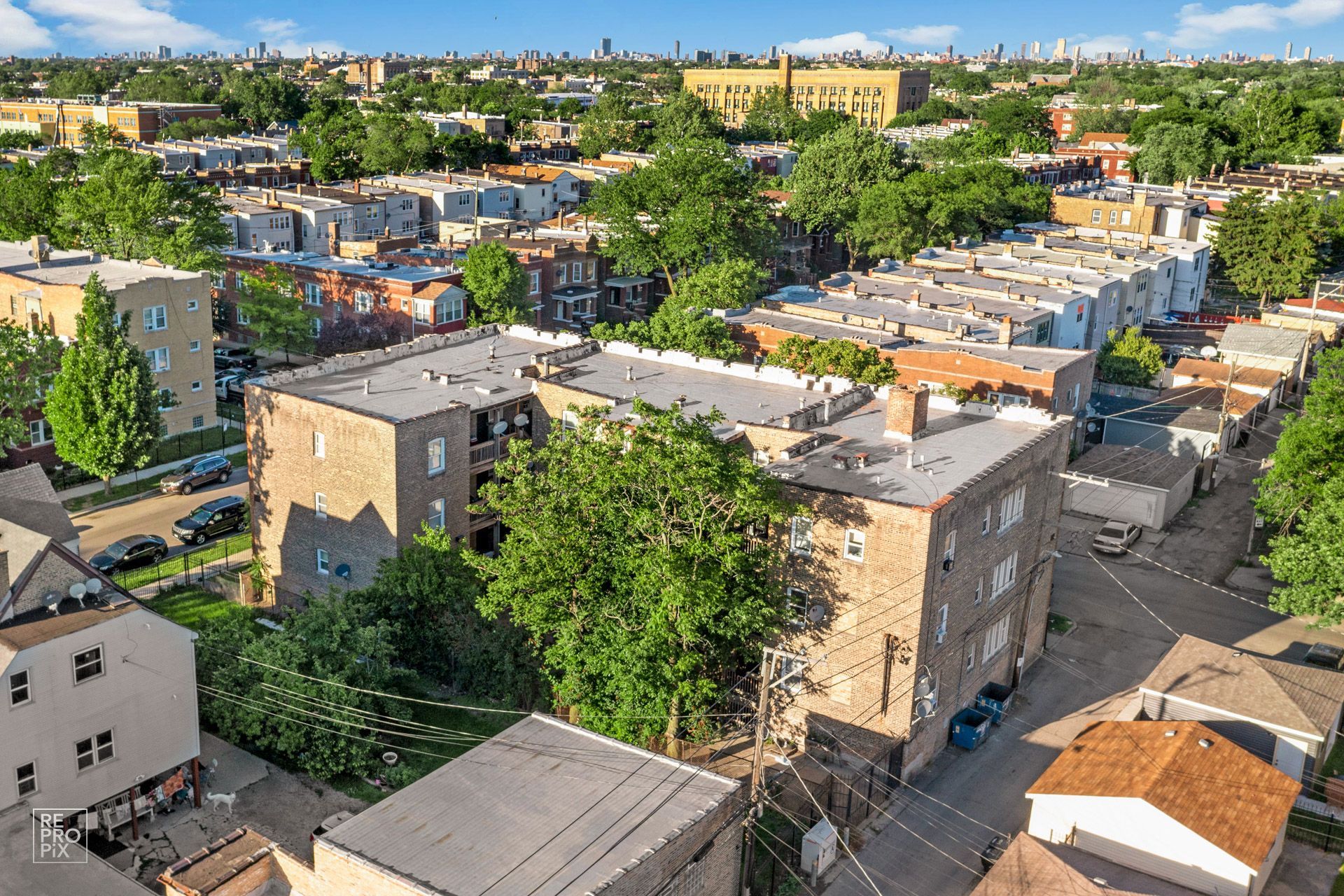 Aerial view of brick apartment buildings in a city neighborhood, surrounded by trees and houses on a sunny day.