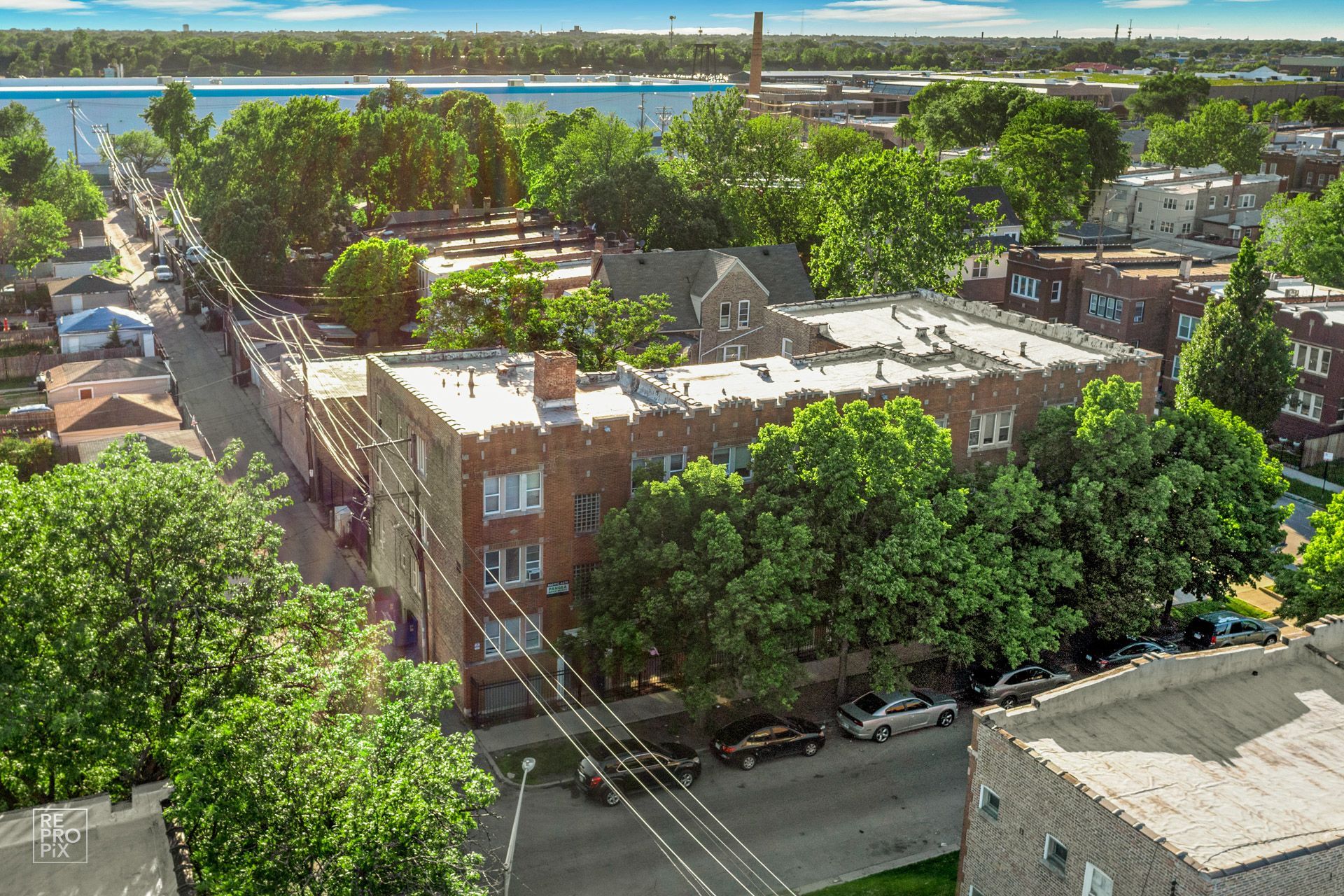 Aerial view of a brick building with a rooftop surrounded by green trees in a residential area.