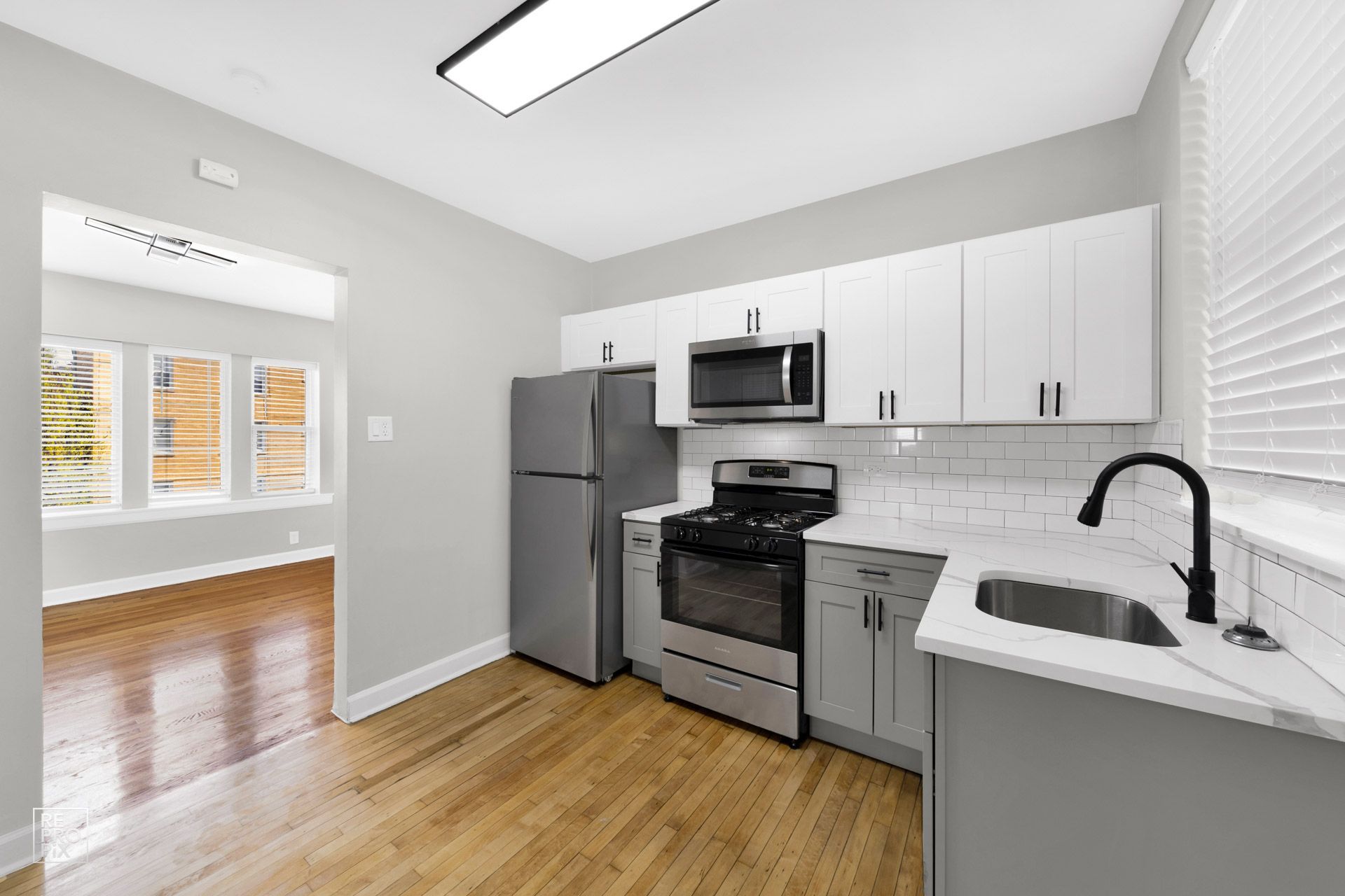 A modern kitchen with stainless steel appliances, white cabinets, and a view into a living space.