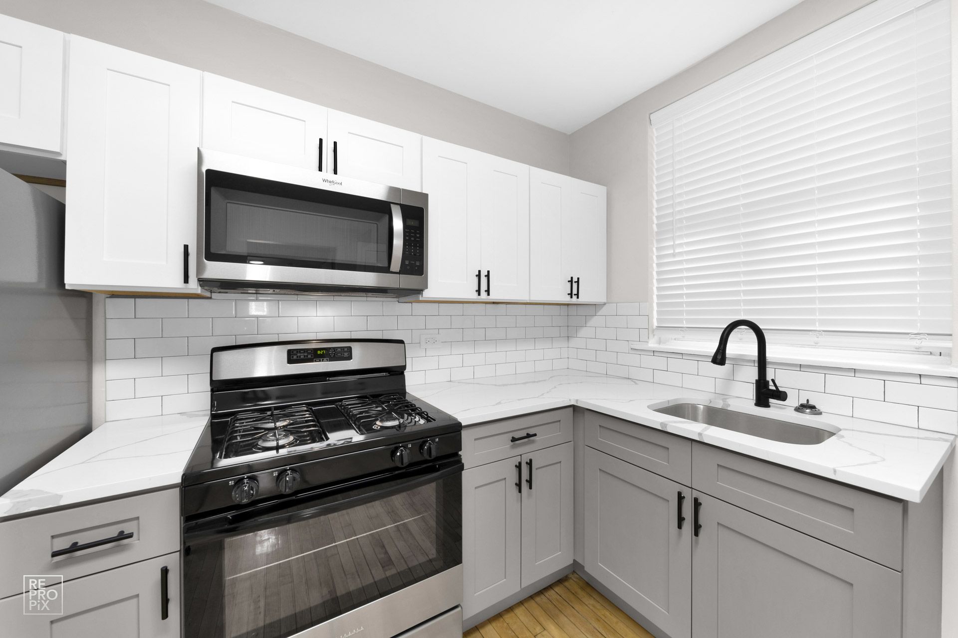 Modern kitchen with white and gray cabinets, stainless steel appliances, and white tile backsplash.