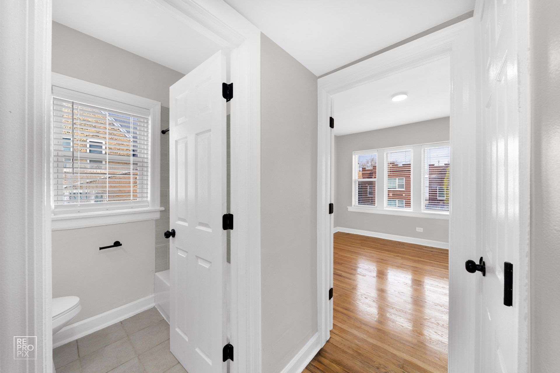 Bathroom doorway leading to a bedroom with hardwood floors. White doors, gray walls, and bright windows.