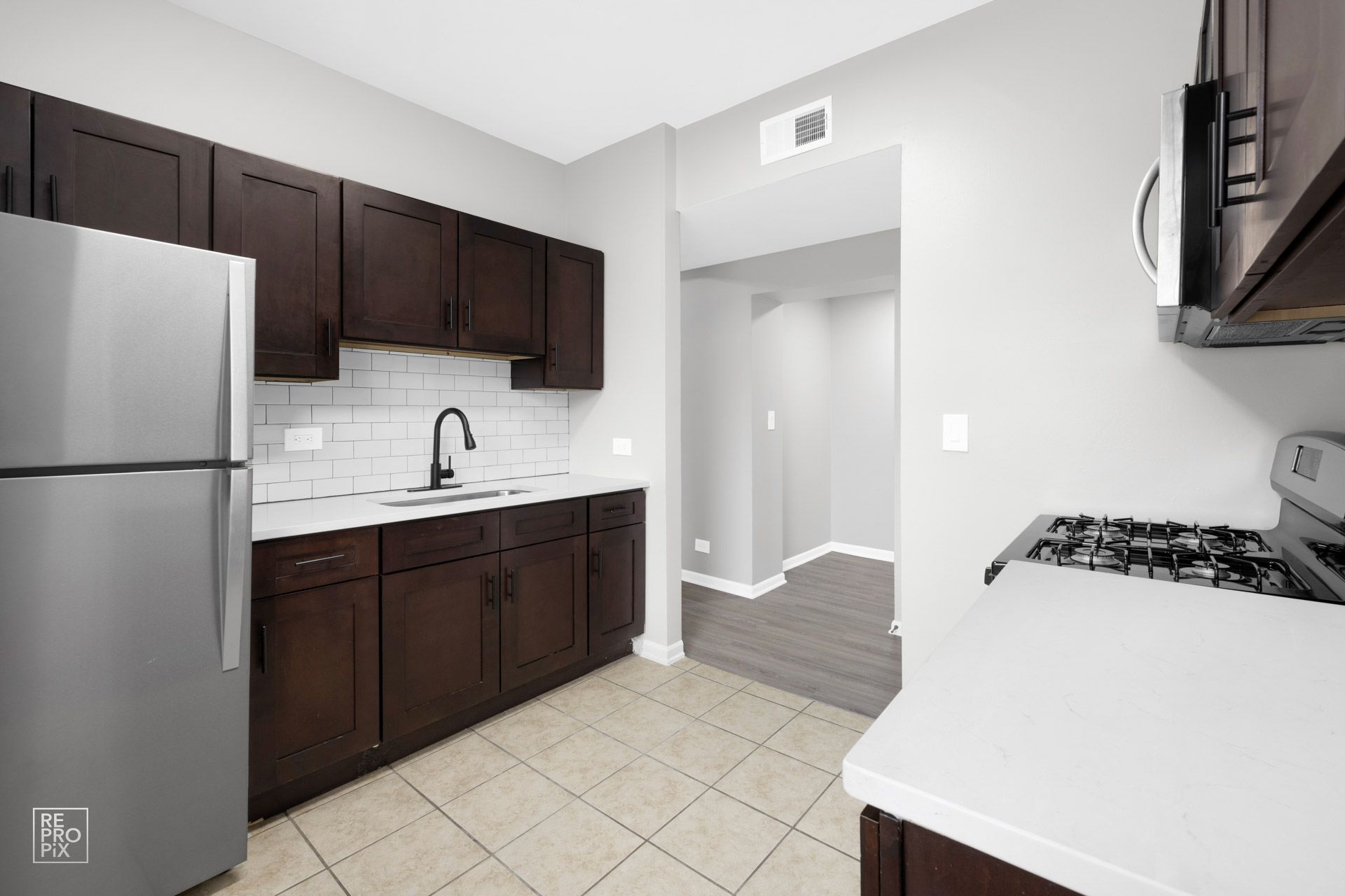 Modern kitchen with dark brown cabinets, stainless steel appliances, and white countertops.