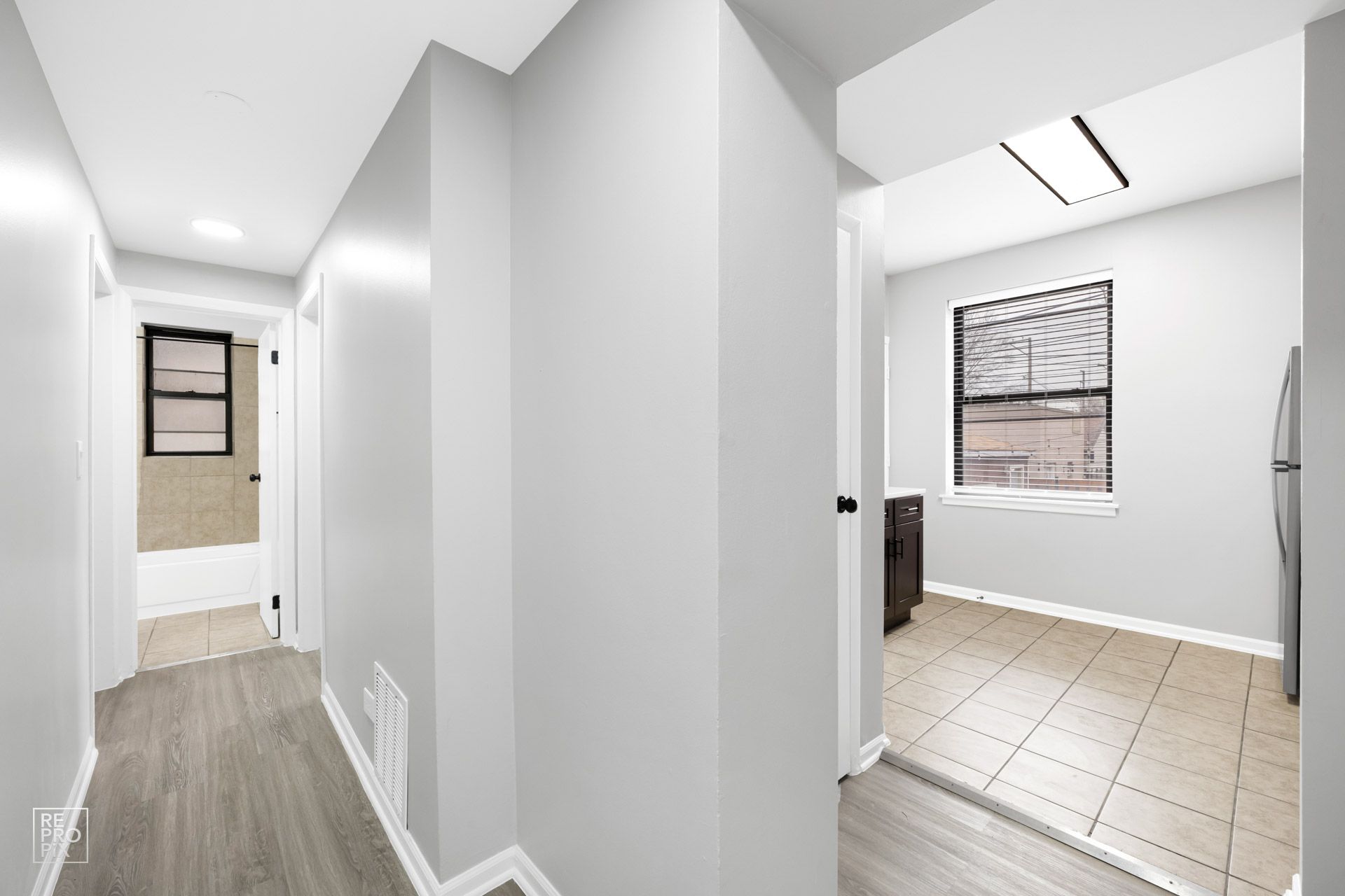 Hallway with light gray walls, wood-look floor, and doorway to a room with a window.