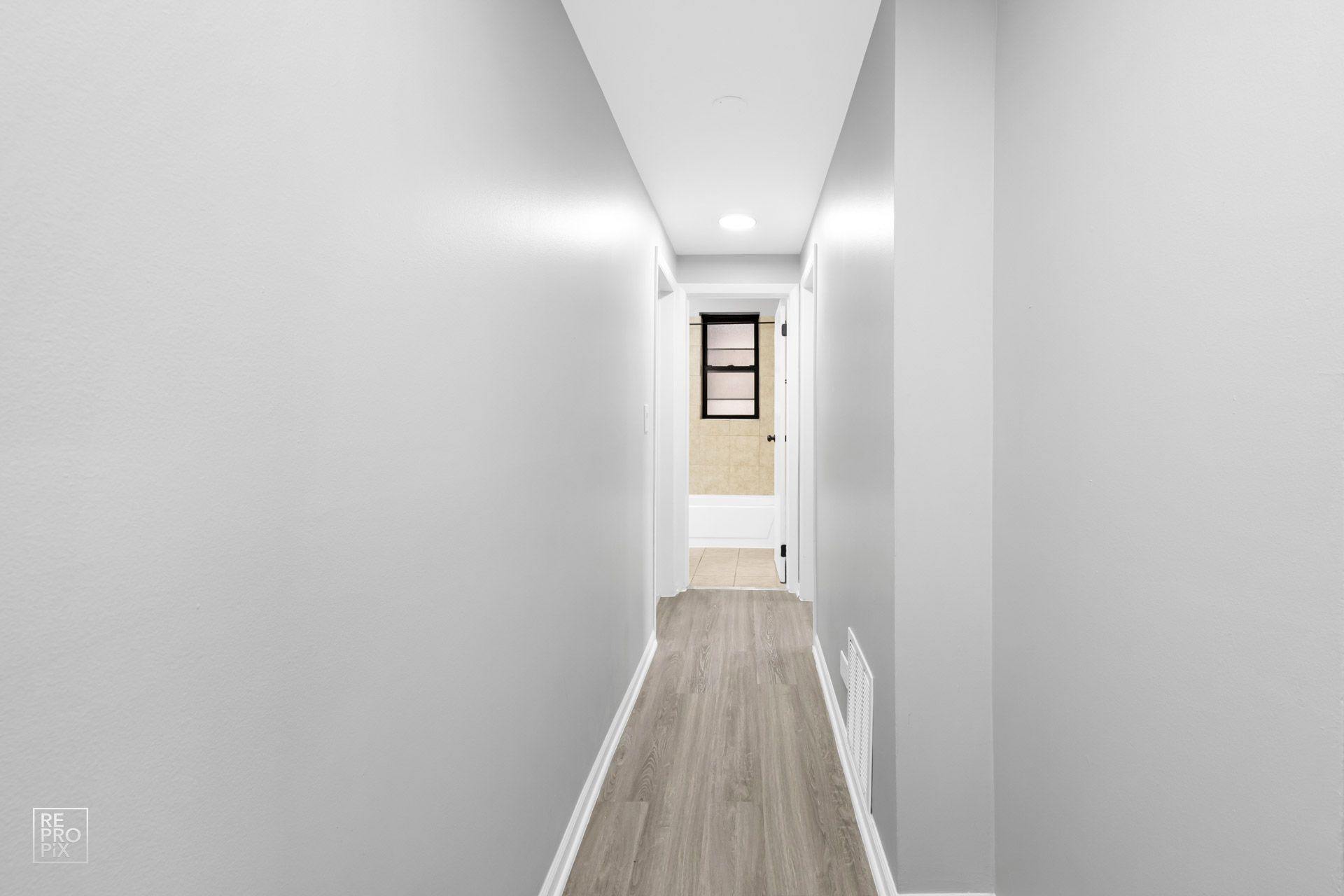 Narrow hallway with gray walls, light wood-look flooring, and a door at the end.